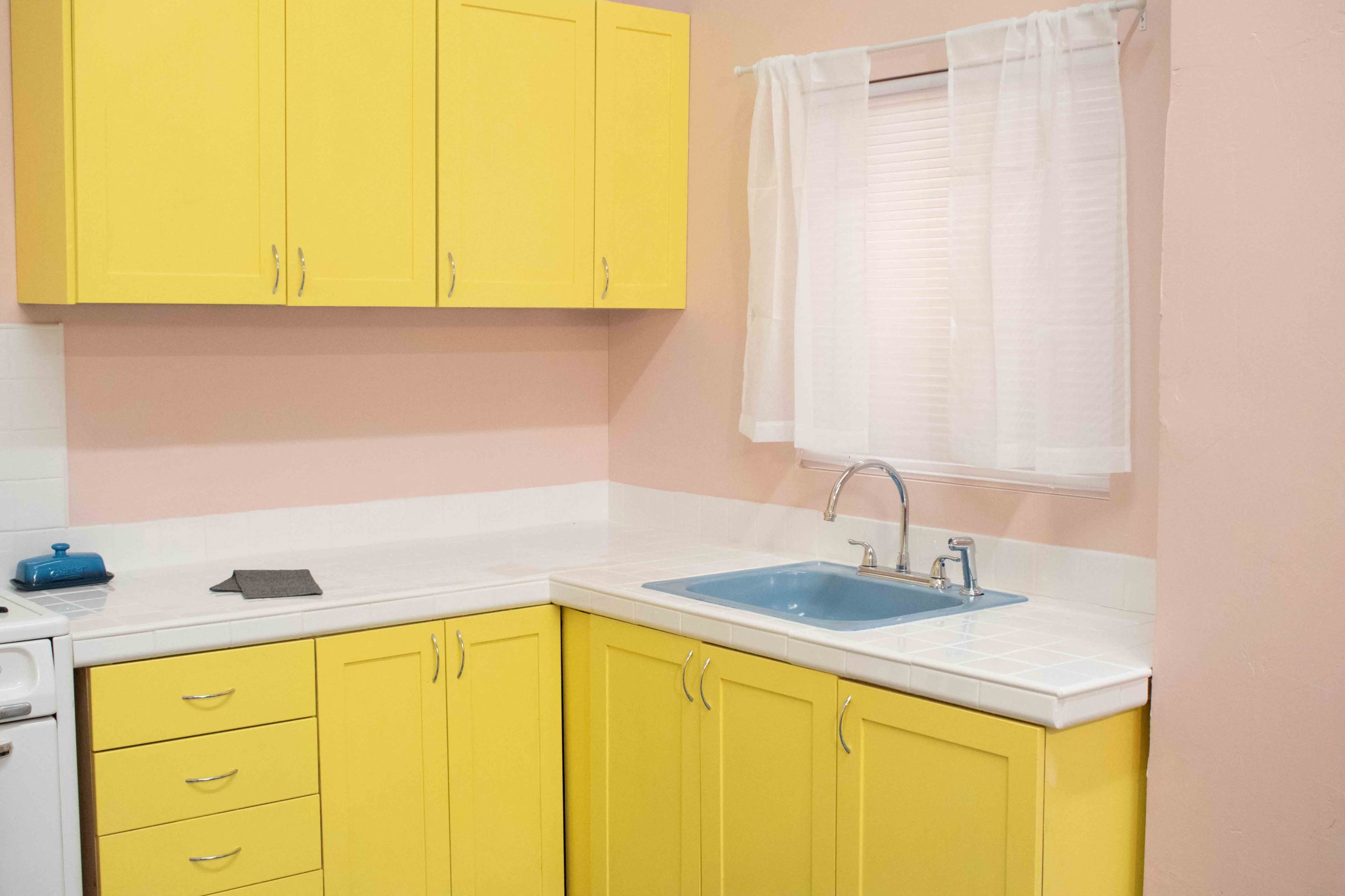 A kitchen featuring yellow cabinets, a blue sink, and a window with white curtains.