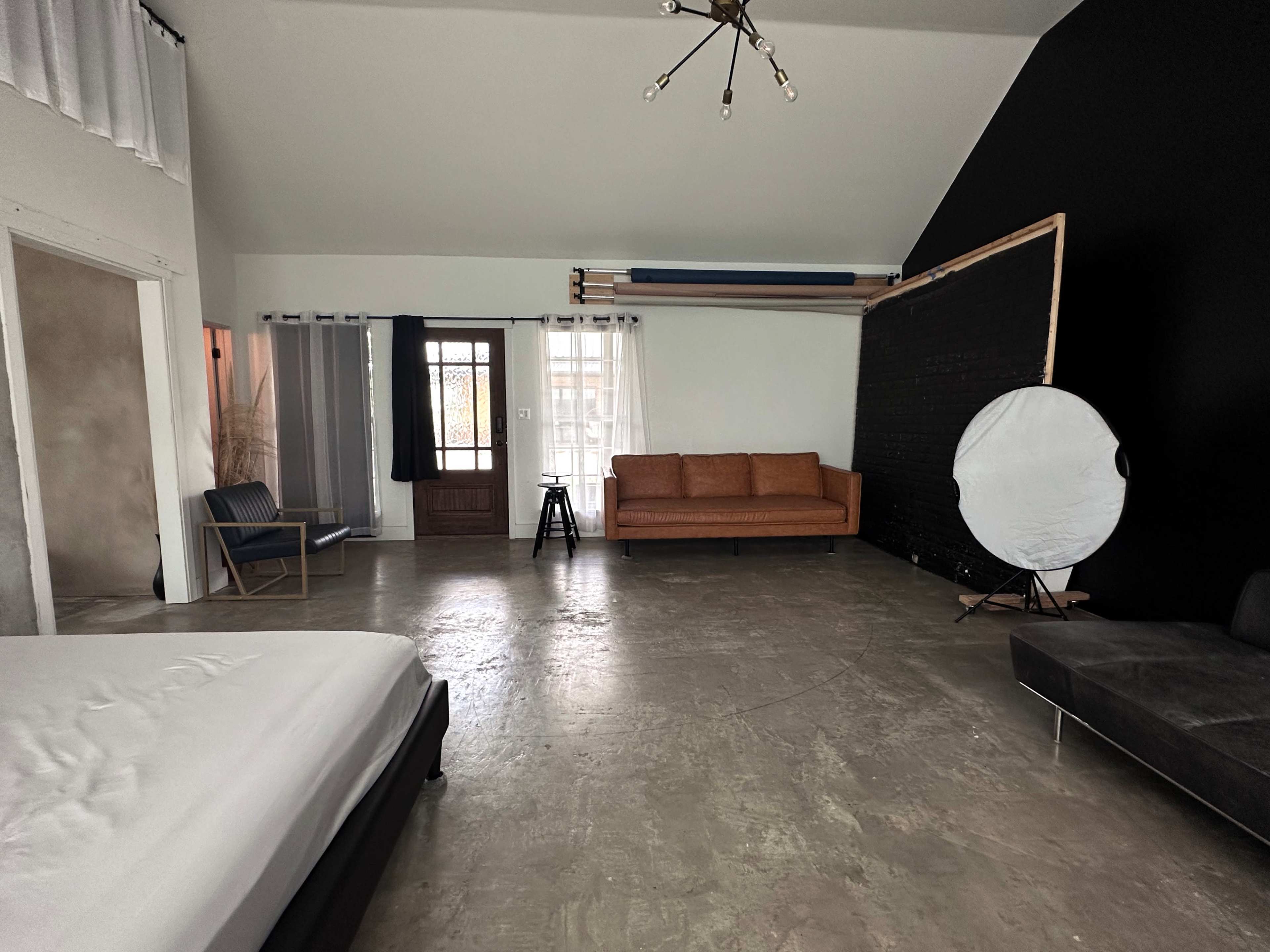 A spacious interior with a large, light-colored room featuring a bed, a brown sofa, and a black accent wall.
