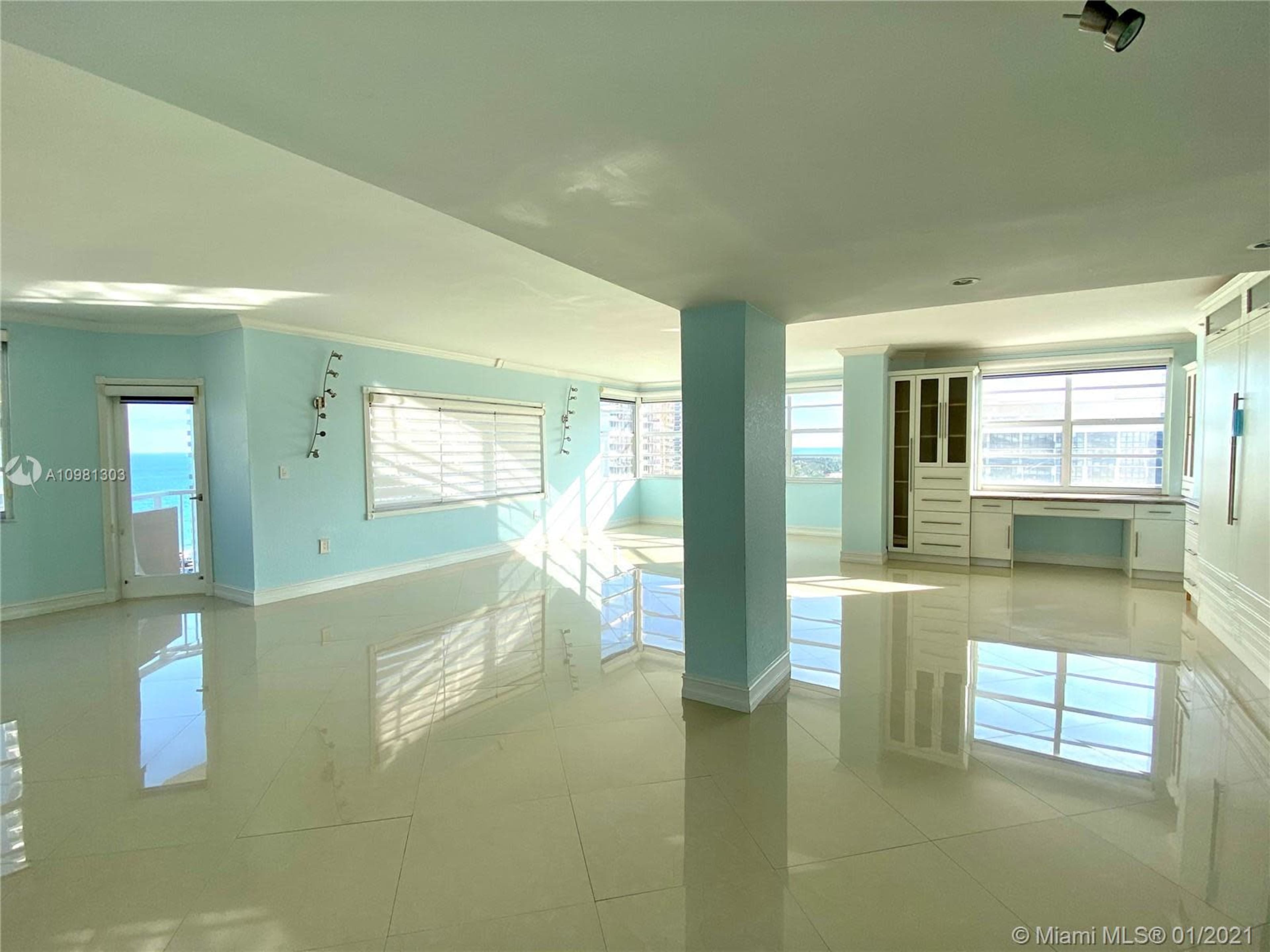 A spacious, light-filled interior of a room with large windows and glossy tile flooring.