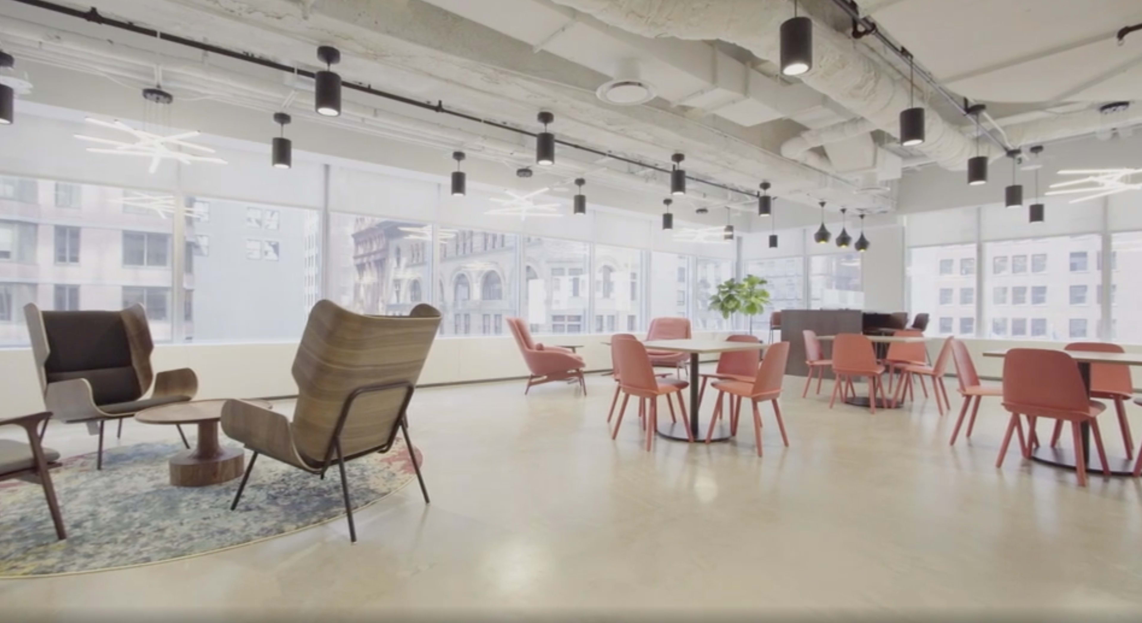 The image shows a modern office space with seating areas that include chairs and tables arranged around large windows.