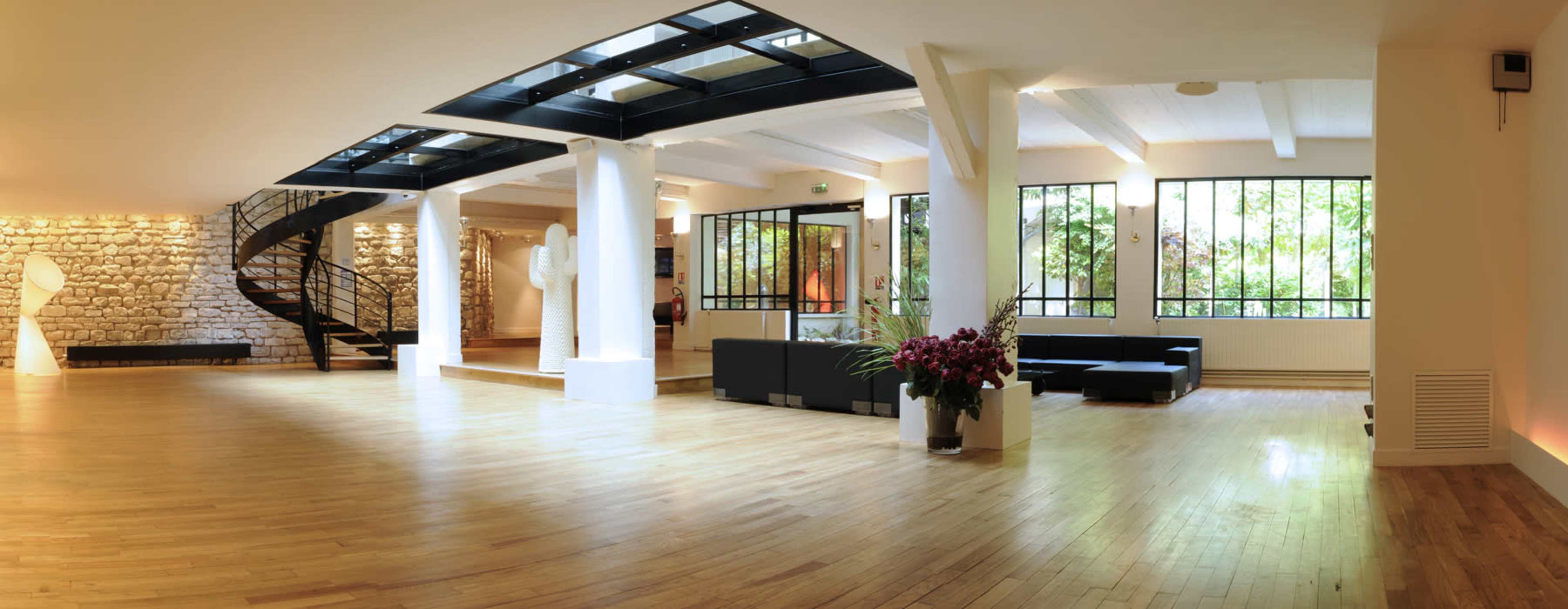 A spacious interior room featuring wooden floors, large windows, and a spiral staircase, complemented by modern furniture and sculptures.