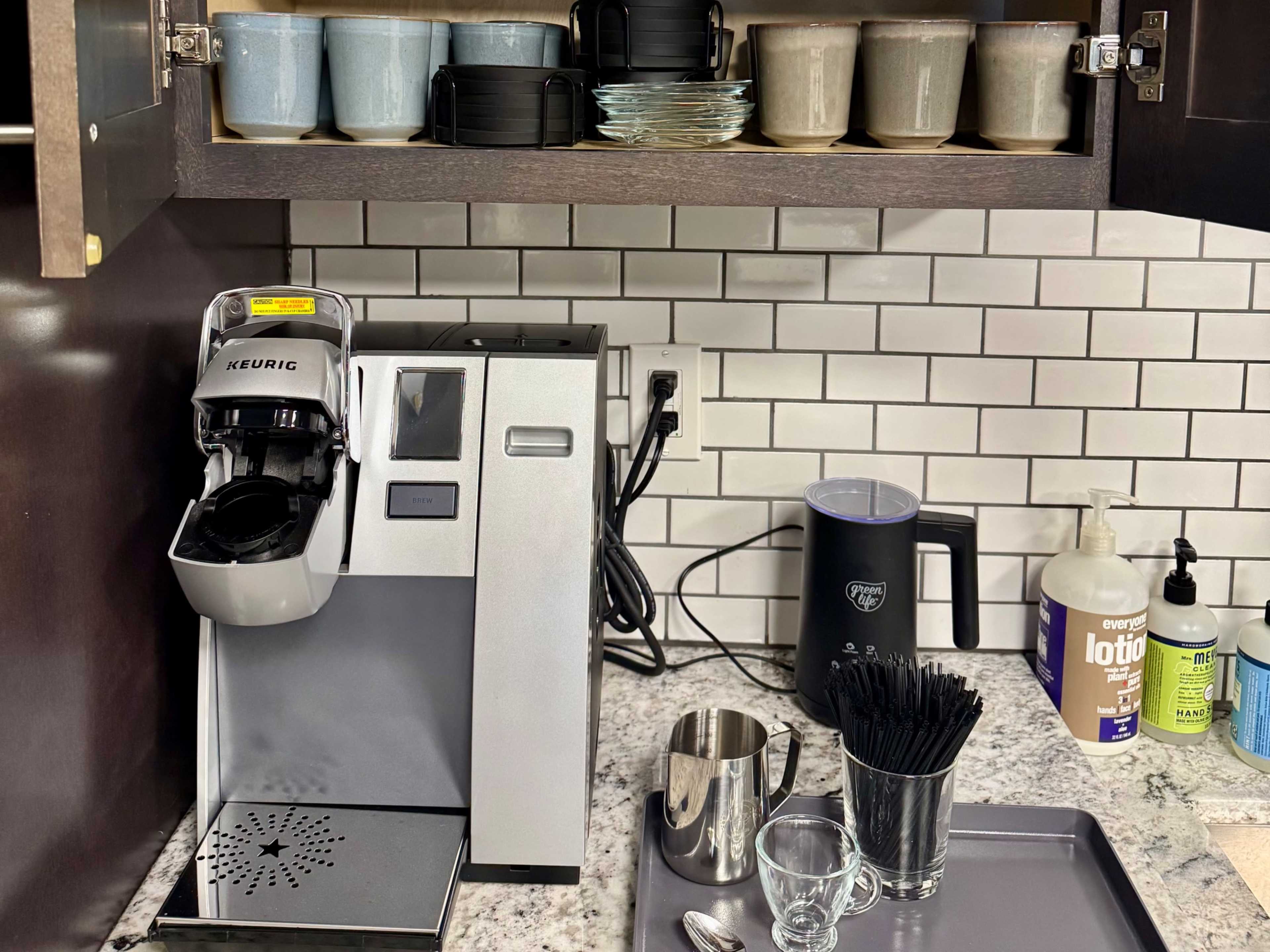 A modern coffee maker is placed on a granite countertop beneath a cabinet with various cups and utensils.