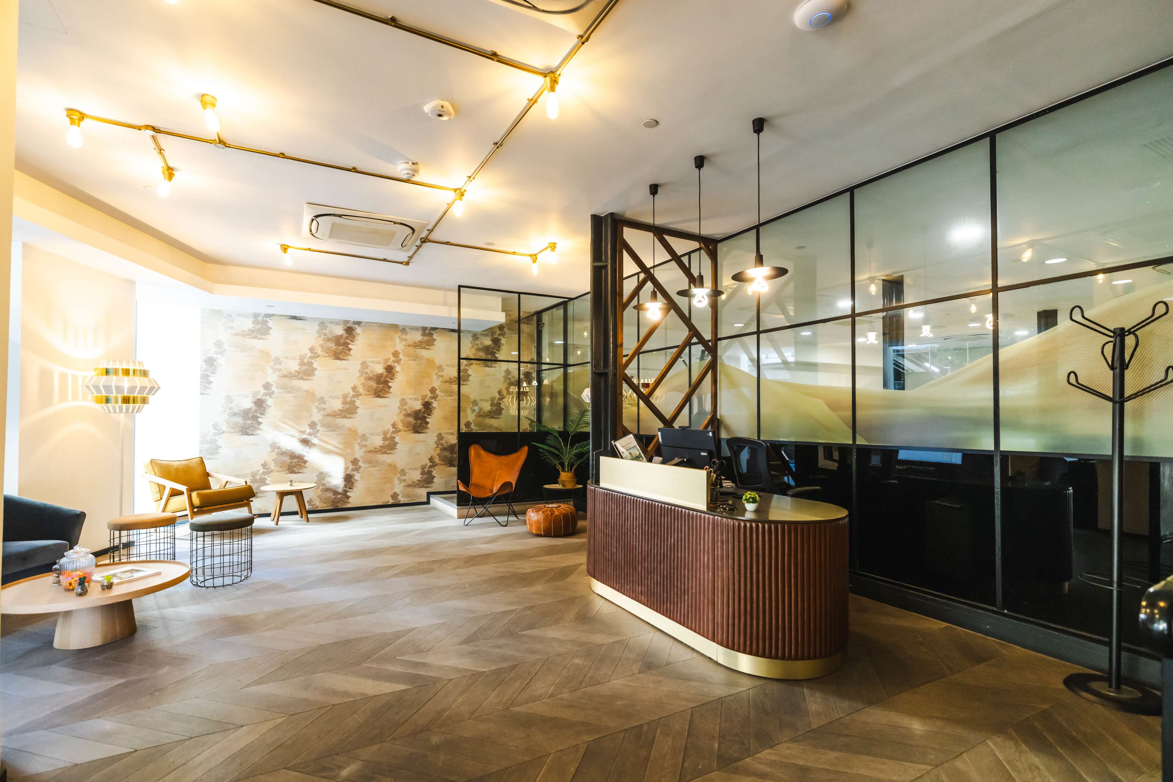 A modern reception area features a wooden front desk, geometric decorations, and a blend of seating options surrounded by large glass panels.