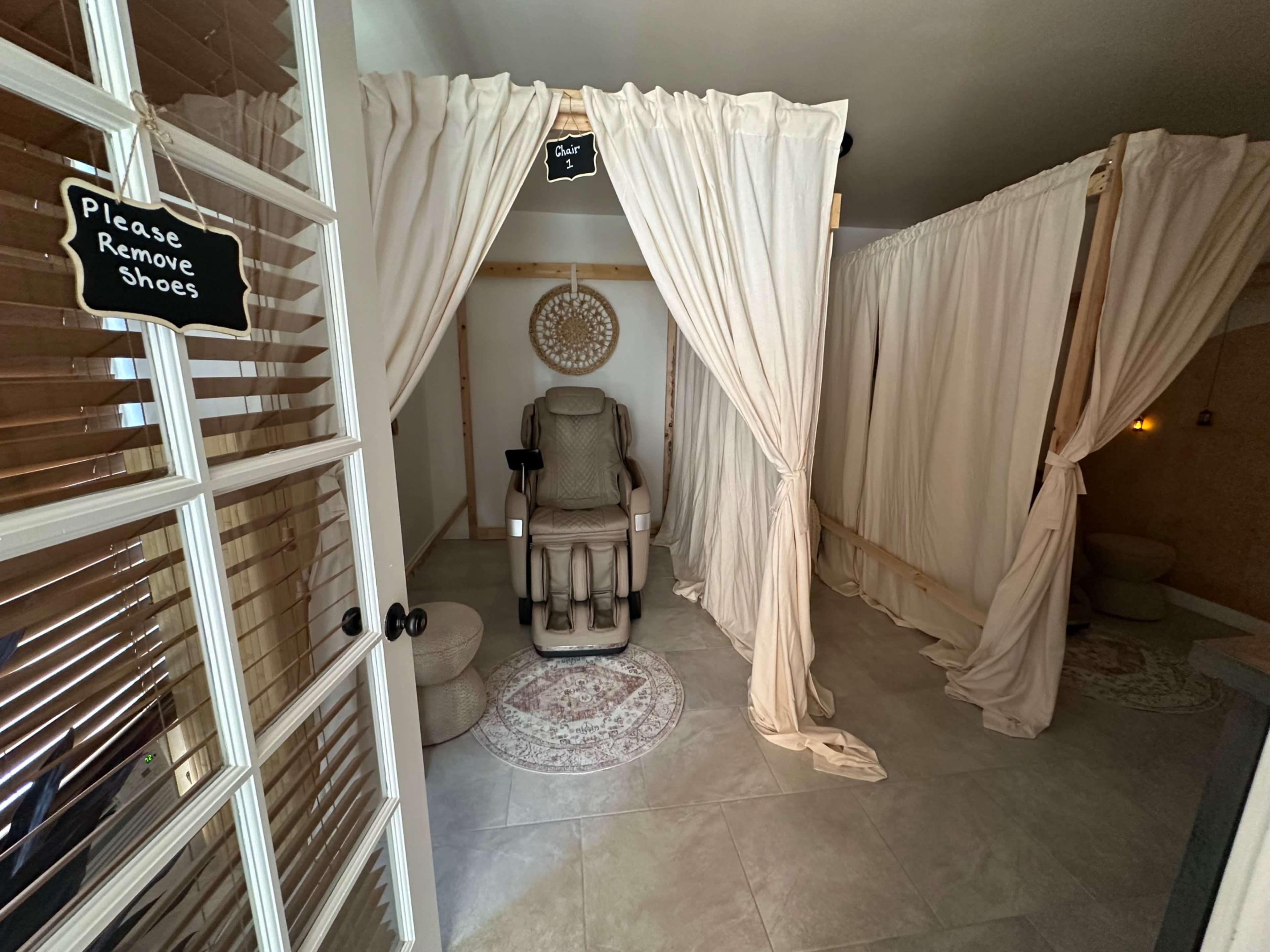The image shows a serene spa room with divided spaces featuring plush chairs and privacy curtains.