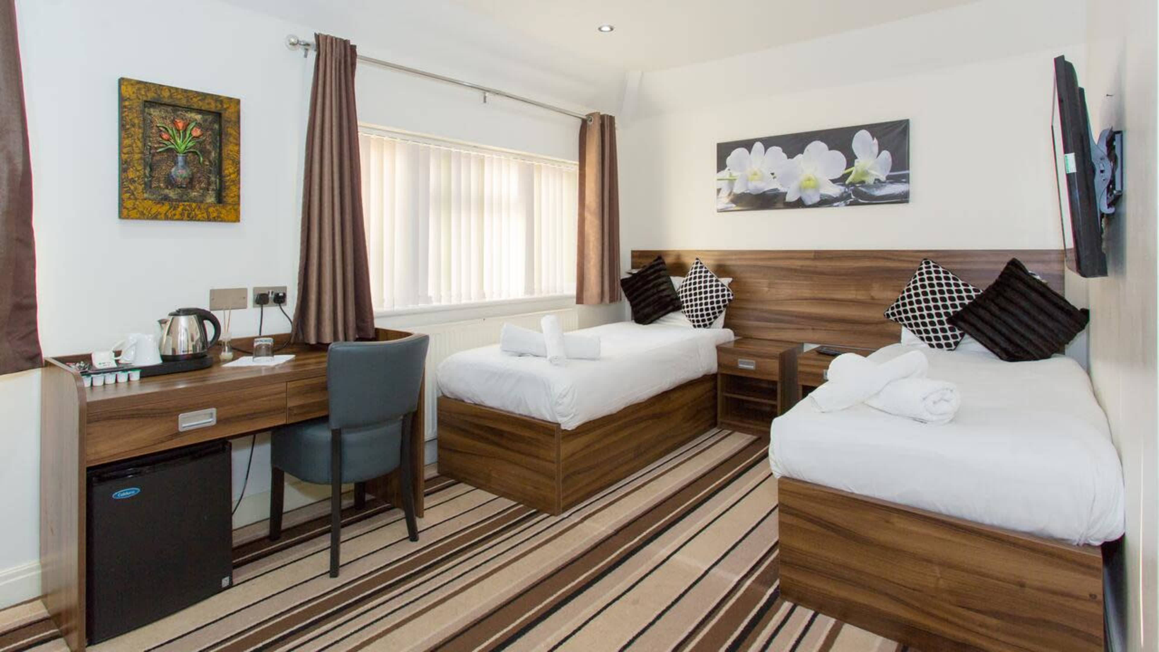 A well-furnished hotel room featuring two single beds, a desk with a chair, and a floral artwork on the wall.