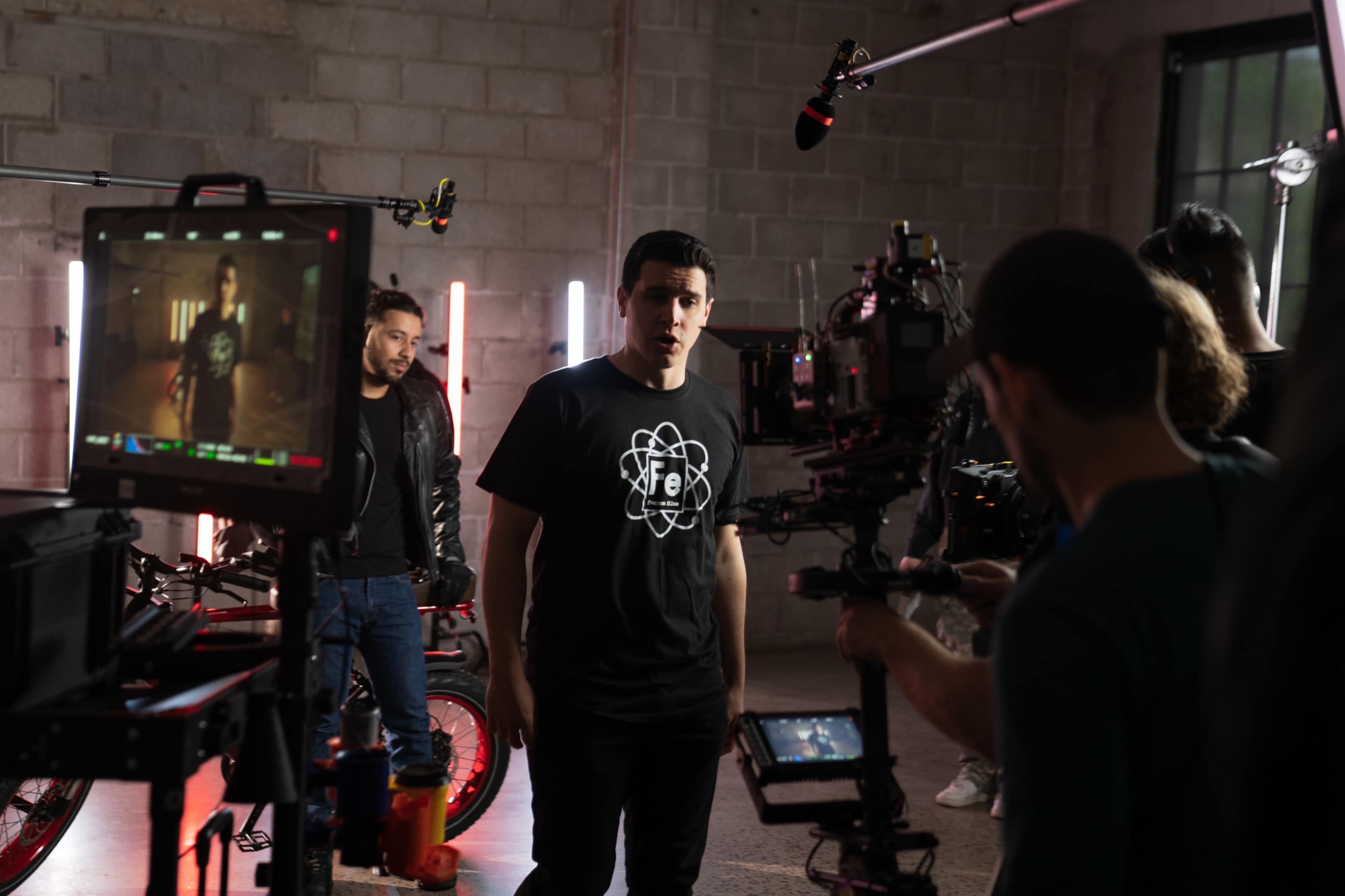 A group of filmmakers is capturing a scene in a studio with neon lighting and a visible camera setup.