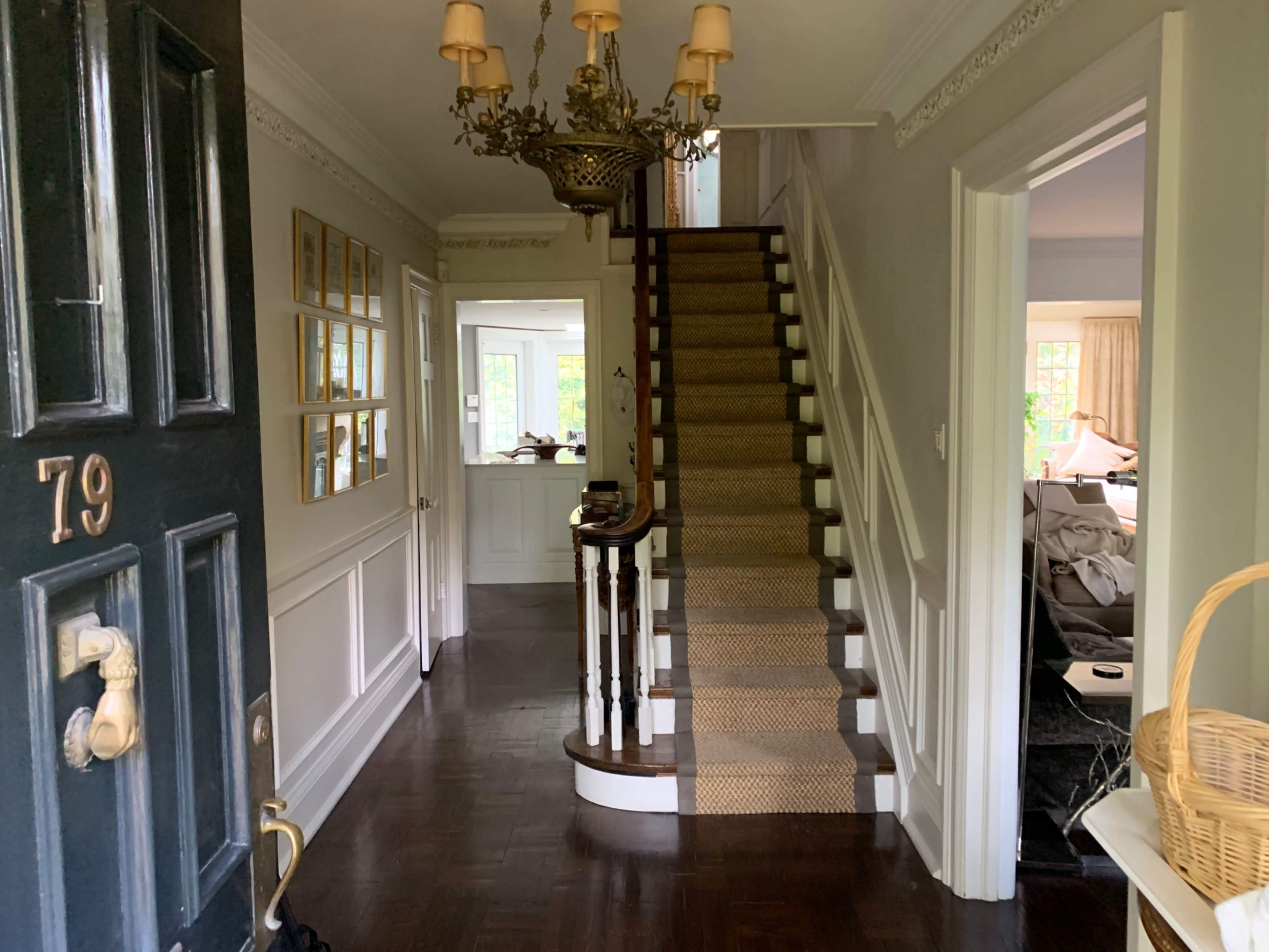A hallway with a staircase leading to the upper floor, framed by decorative wall elements and a chandelier overhead.