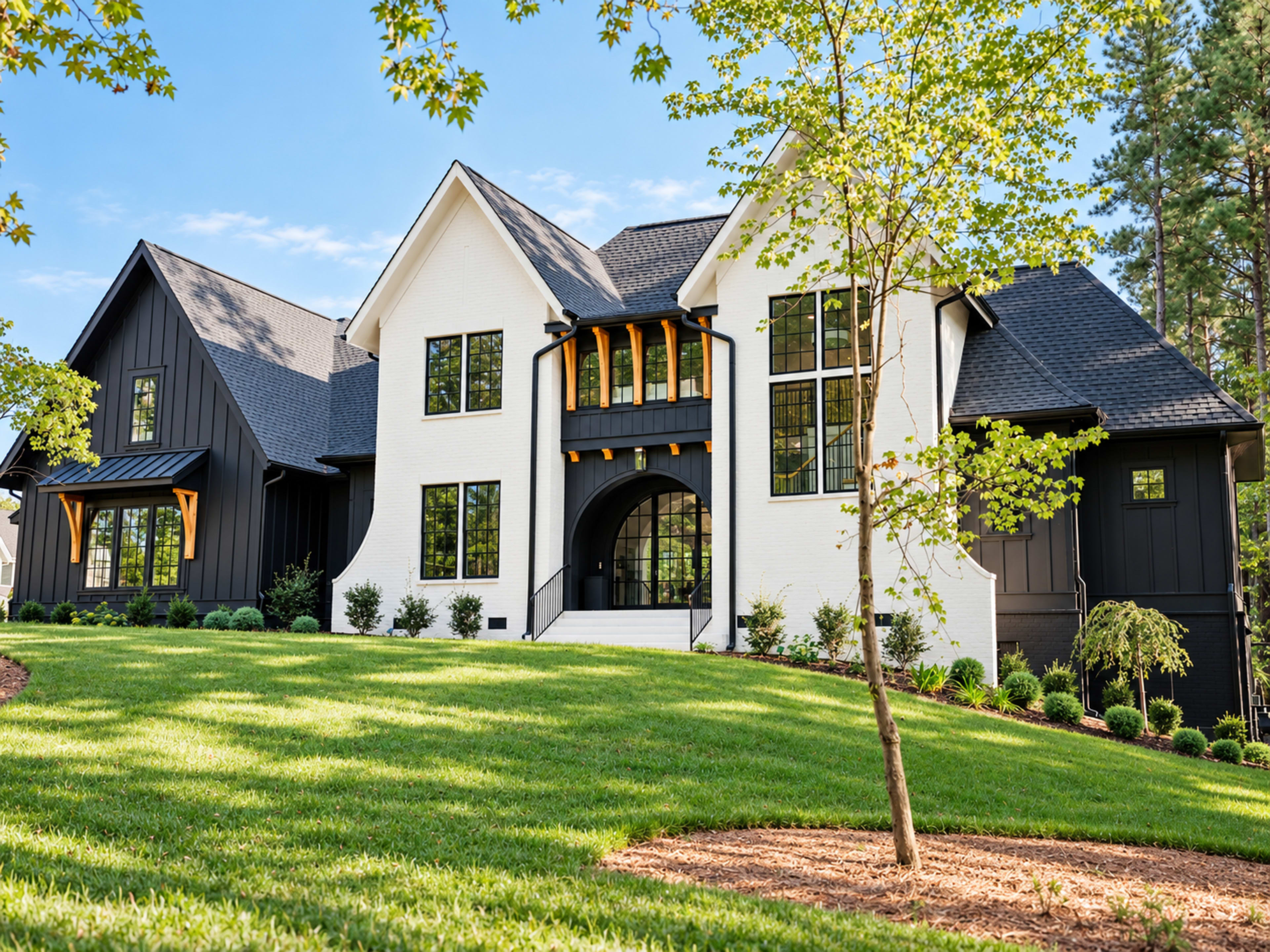The image shows a modern two-story house with a mix of white and black siding, large windows, and a landscaped front yard with green grass and trees.