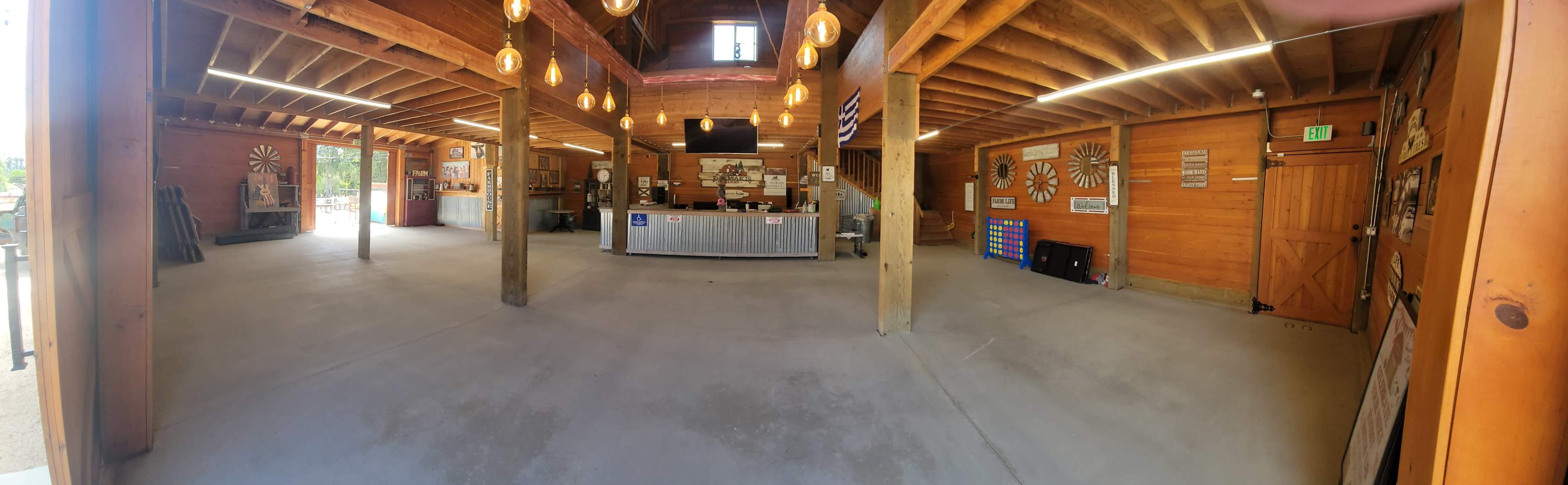 A spacious wooden interior of a building with a counter, several light fixtures hanging from the ceiling, and various decorations on the walls.