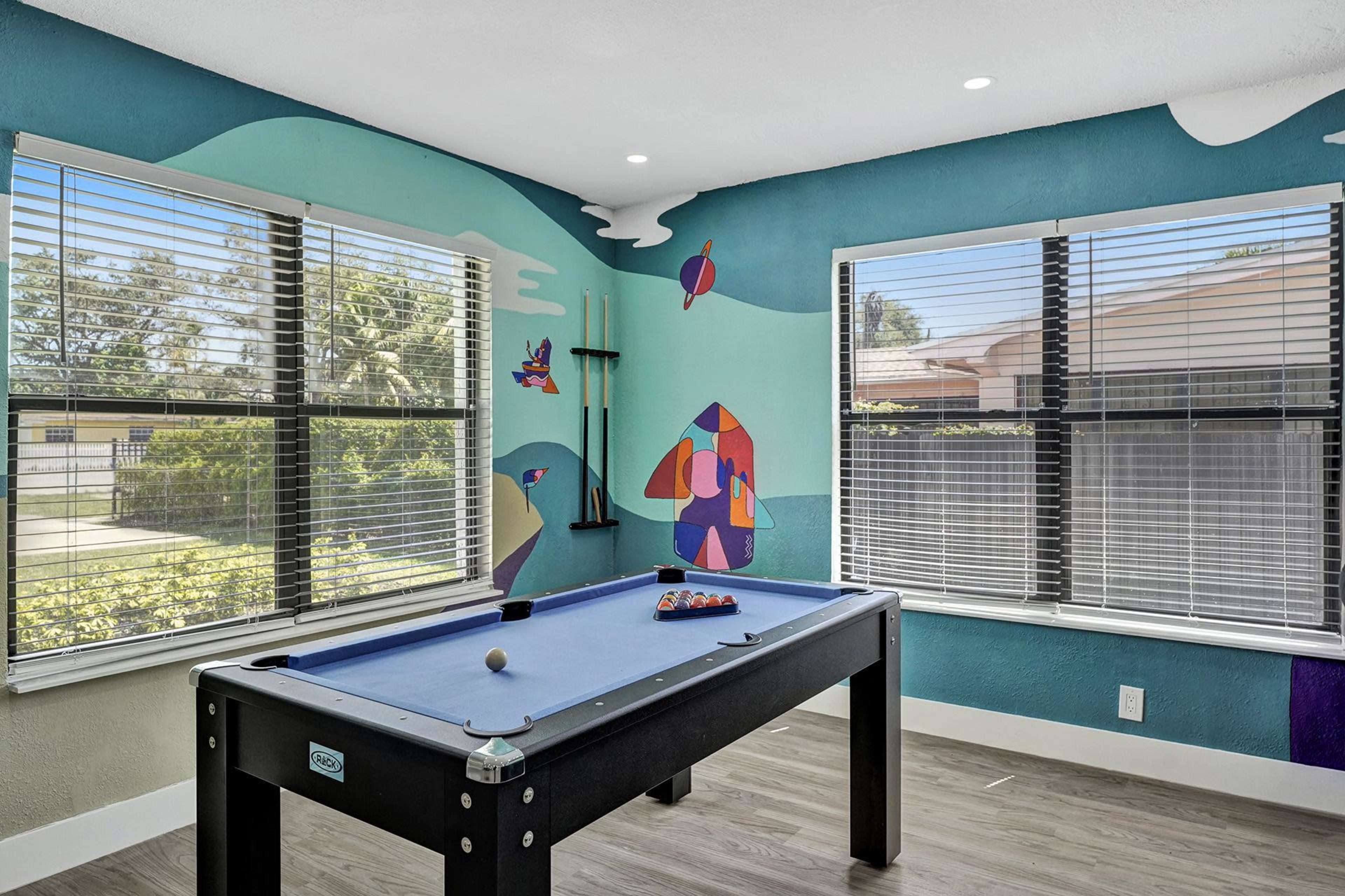 A brightly colored game room with a pool table under natural light coming through large windows.