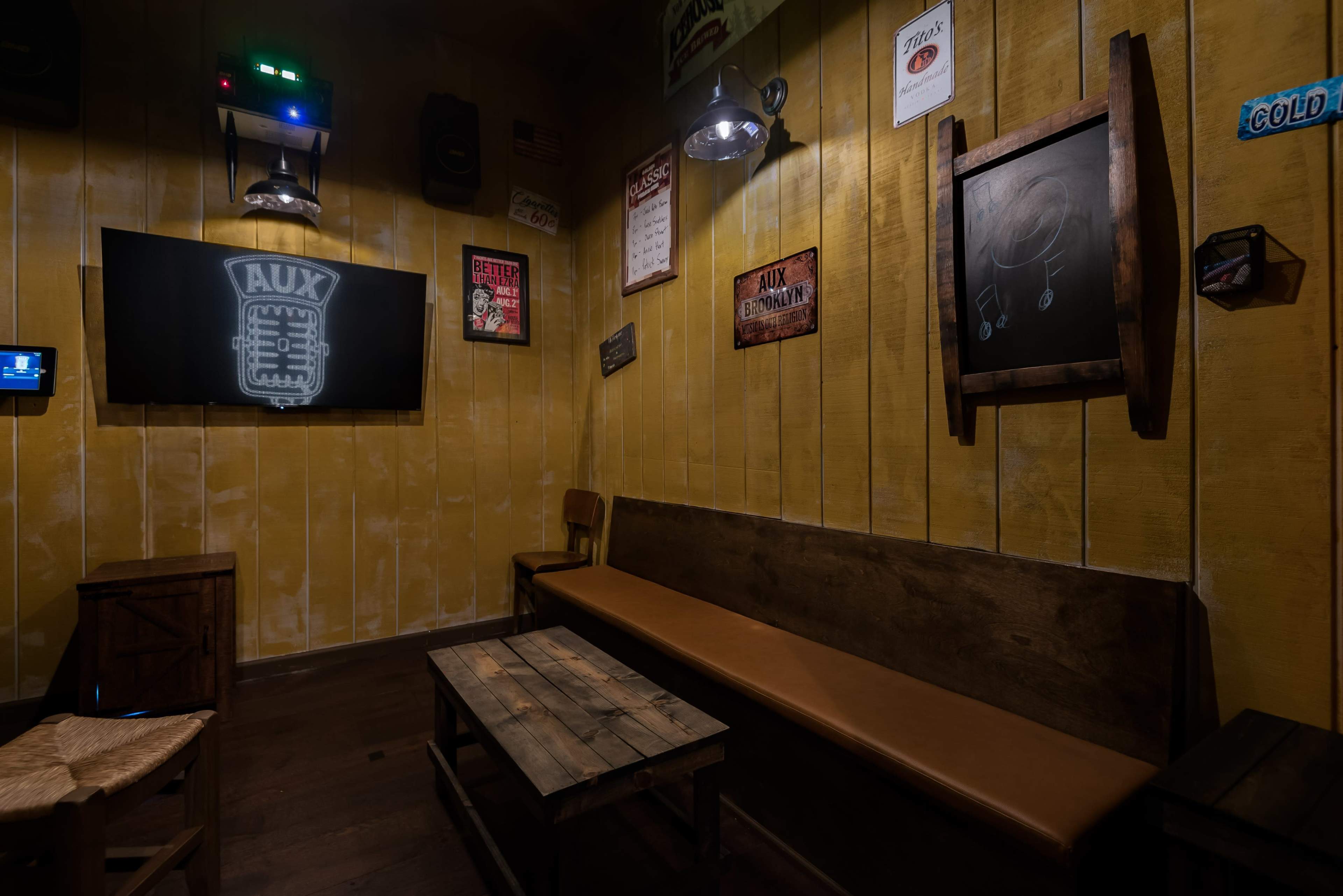 The image shows a cozy room with yellow walls, featuring a wooden bench, a low table, and a chalkboard, accented by various retro signs and a microphone graphic projected on the wall.