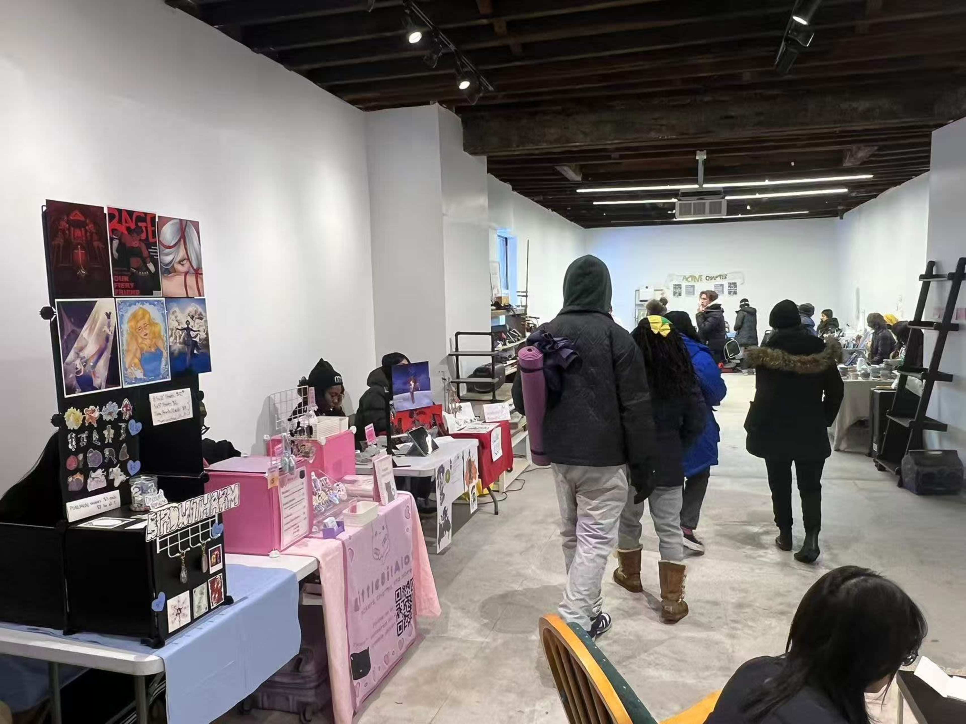 A group of people walks through a spacious indoor market featuring various vendor booths displaying art and handmade items.