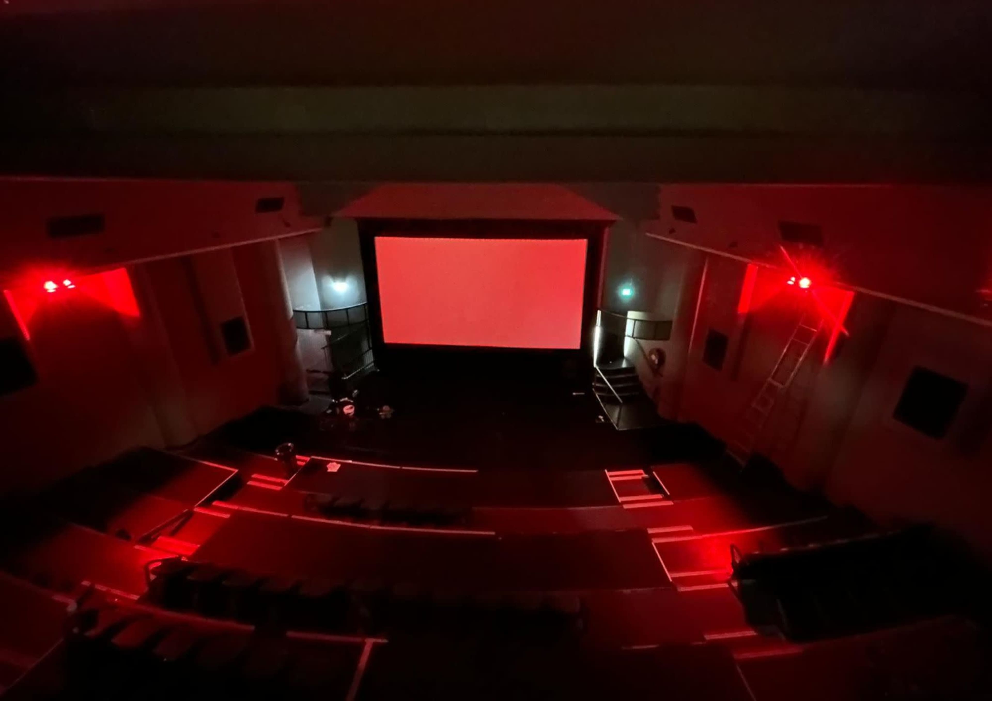 A nearly empty theater with red lighting and a blank screen is visible from an elevated perspective.