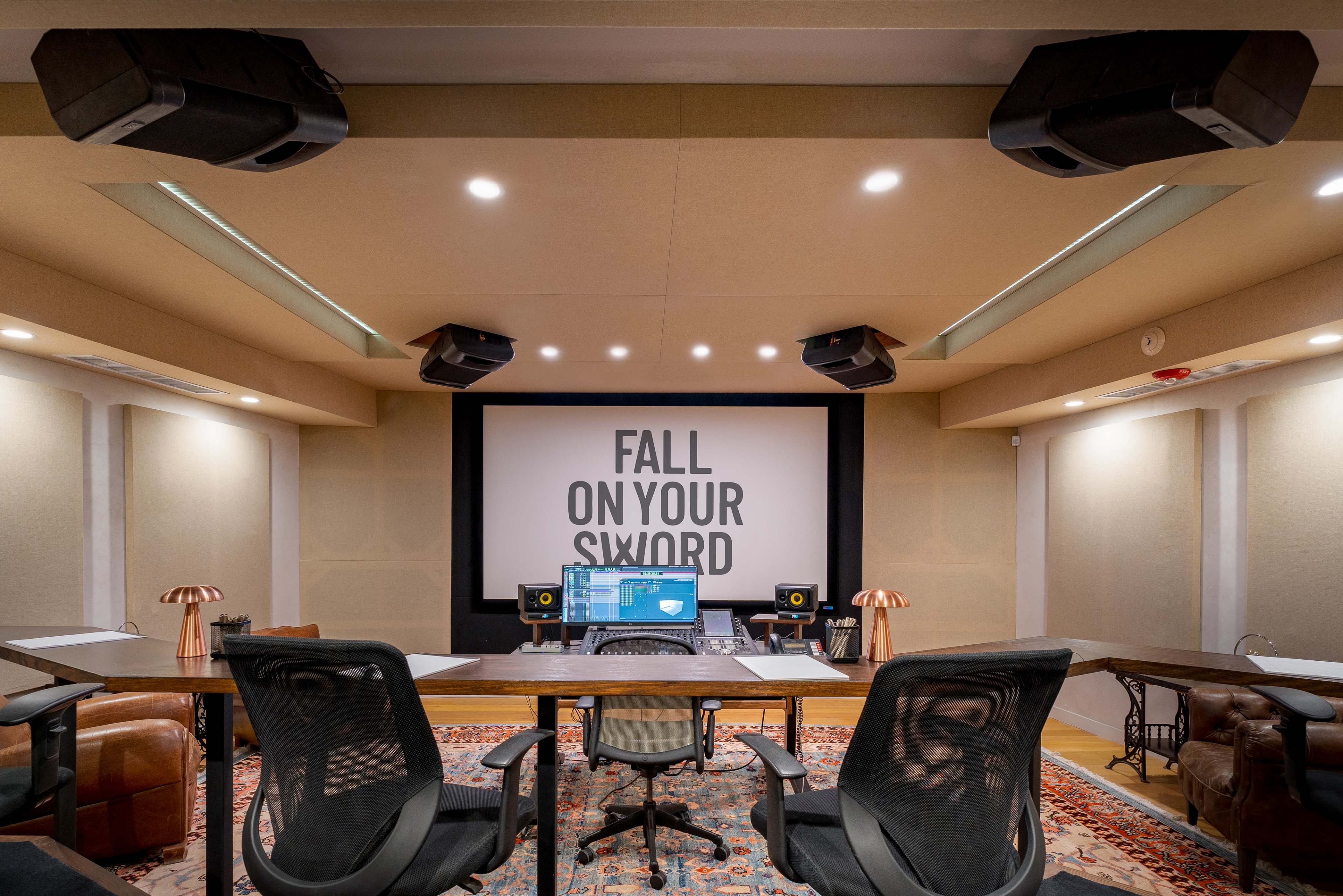 A modern recording studio with a central desk, audio equipment, and a large screen displaying the phrase "FALL ON YOUR SIXTH."