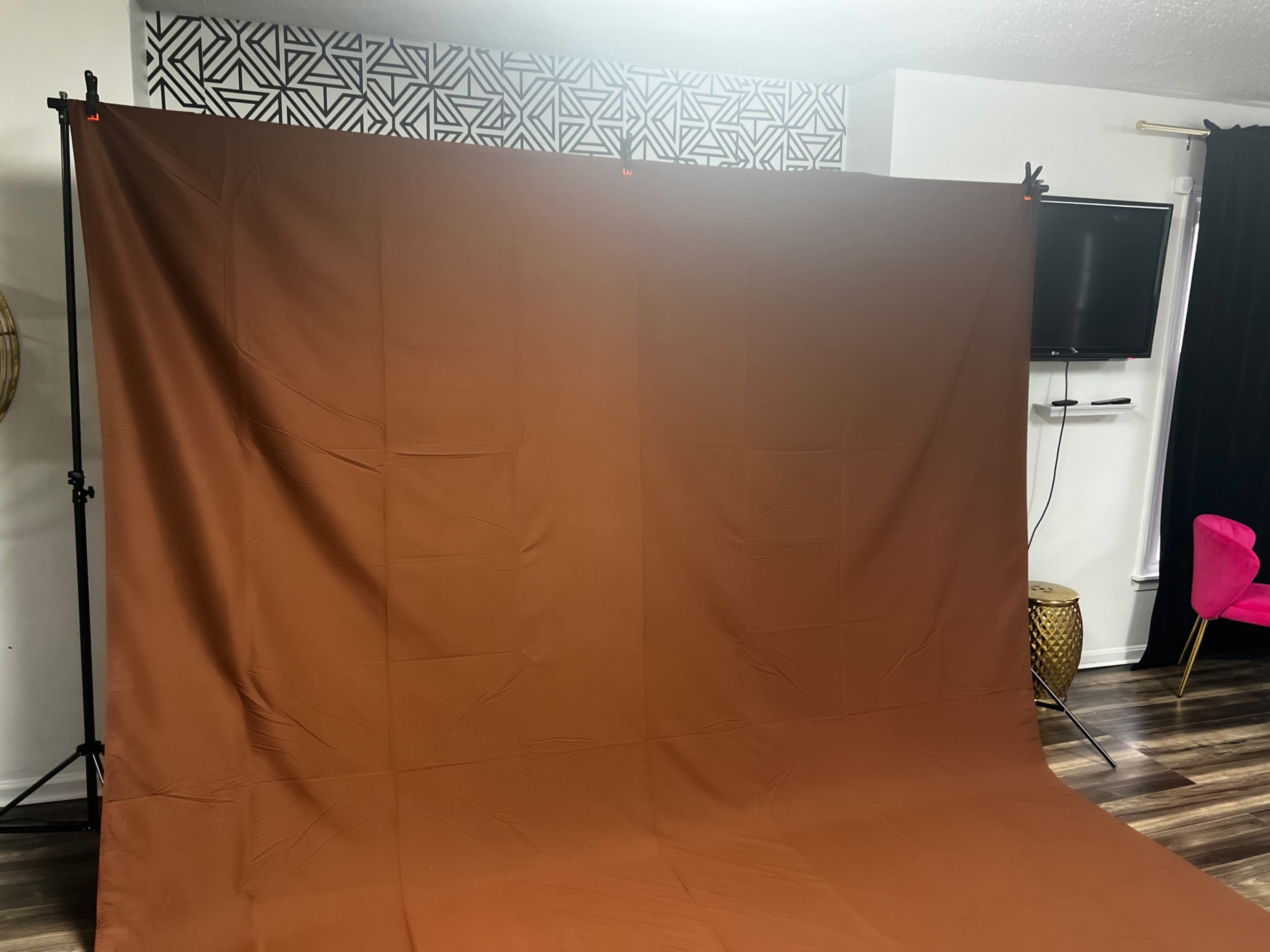 A studio setup featuring a large brown backdrop on a supporting frame, with a television and decorative elements in the background.