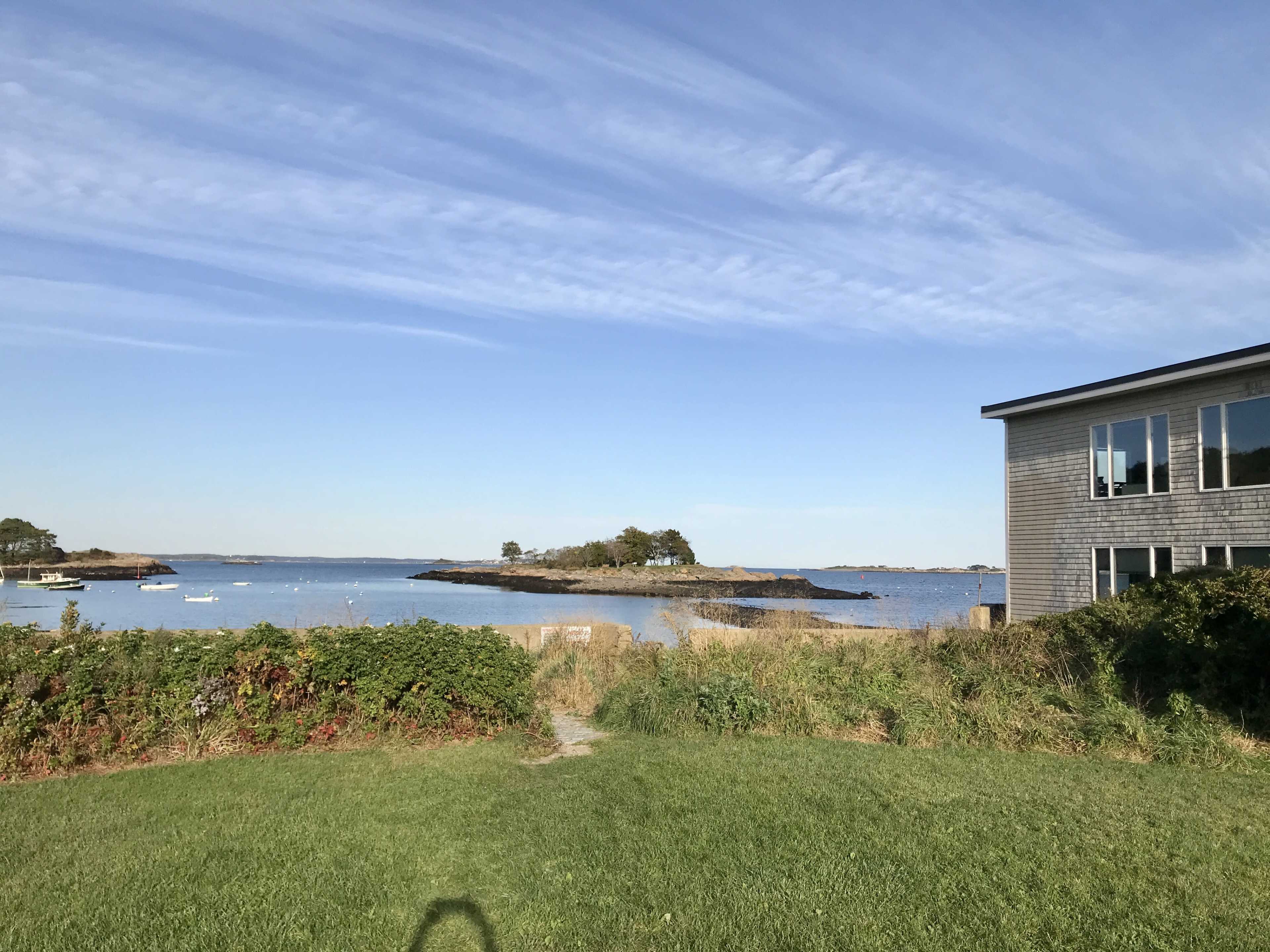 A grassy area leading to a calm coastal scene with water, small islands, and a modern building on the right.