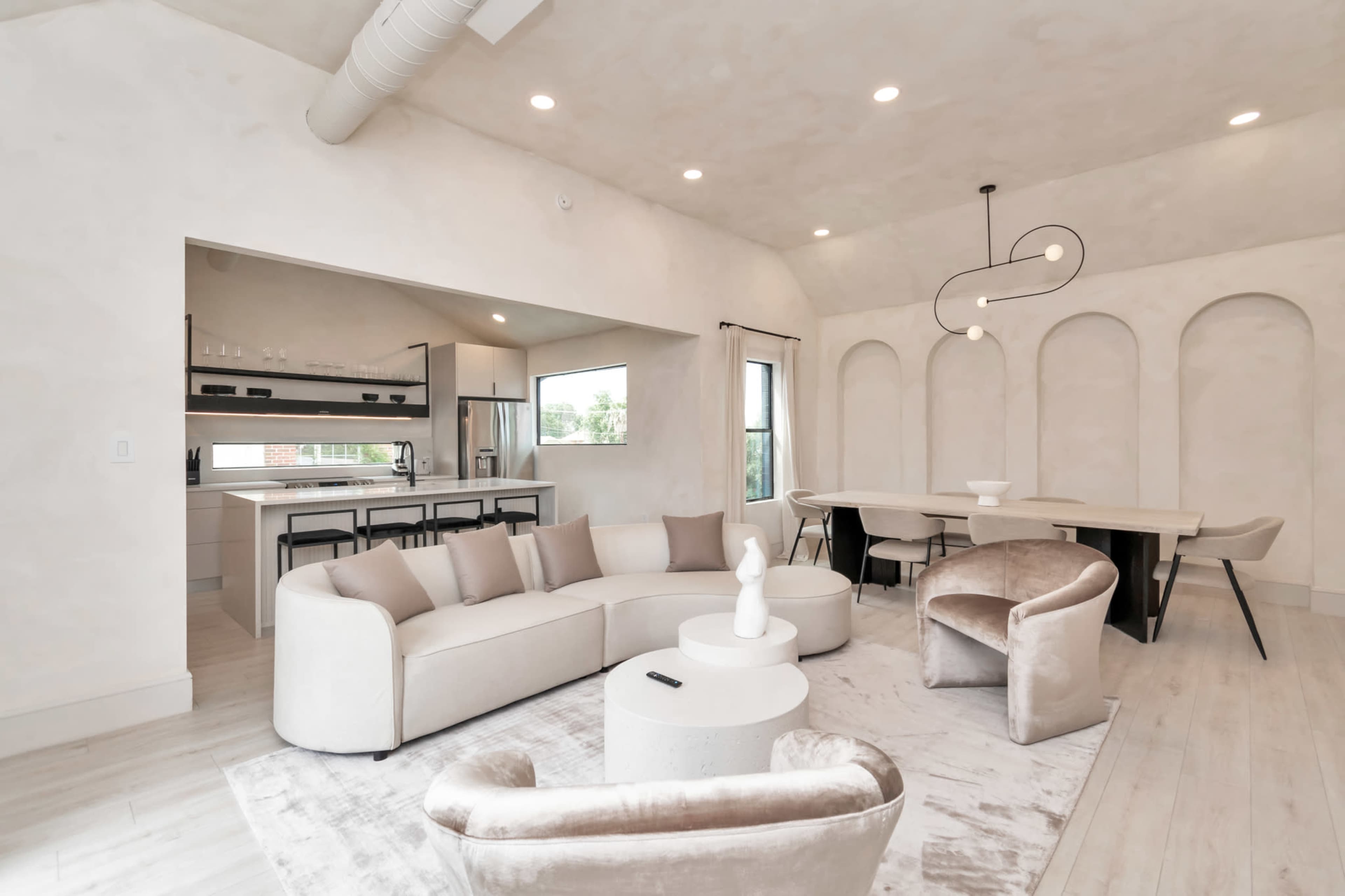 A modern, open-concept living space with a circular sofa, a dining area, and soft lighting highlighting the walls and furniture.