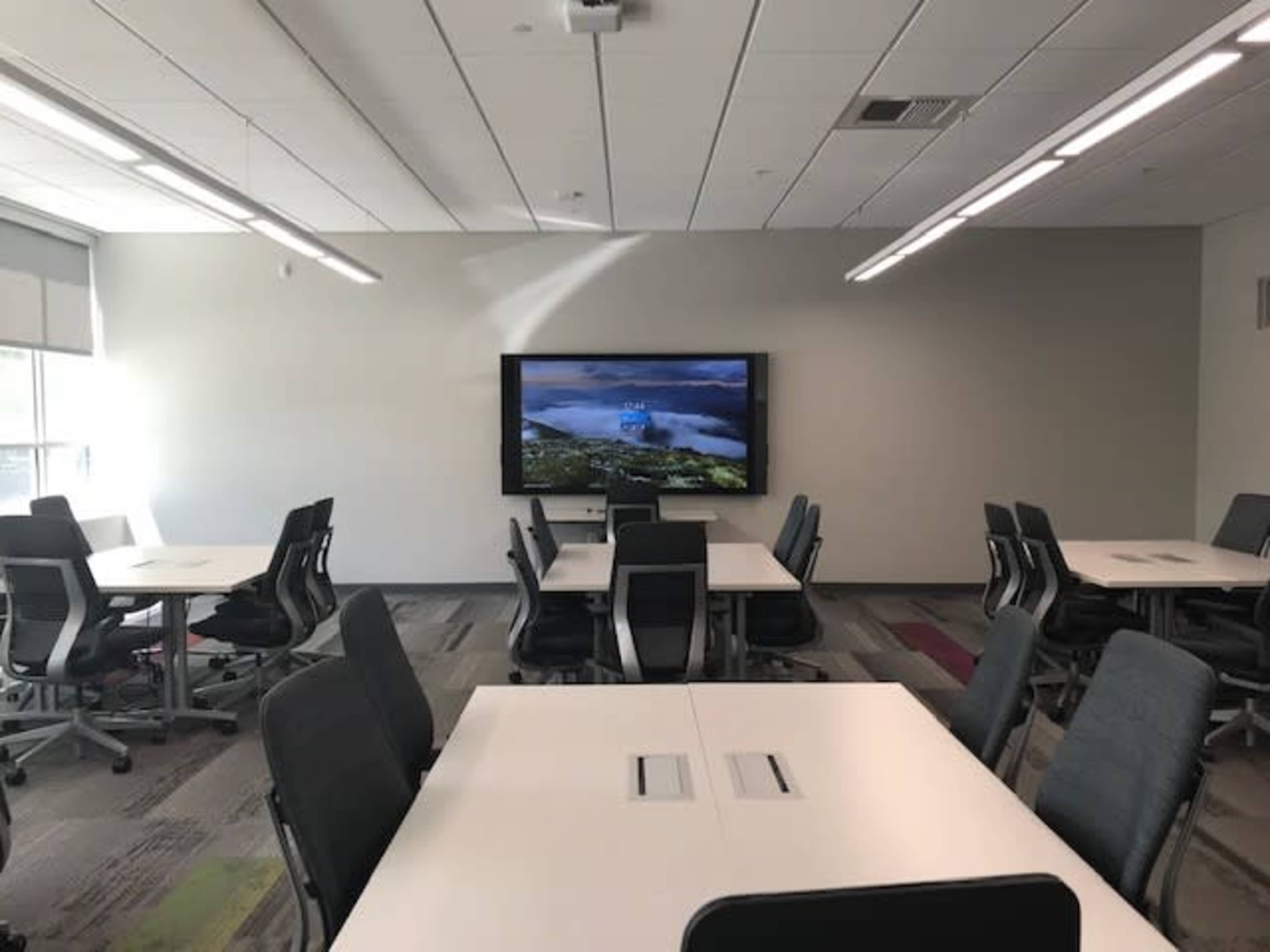 A modern conference room with multiple tables and chairs arranged around a large screen displaying a scenic landscape.