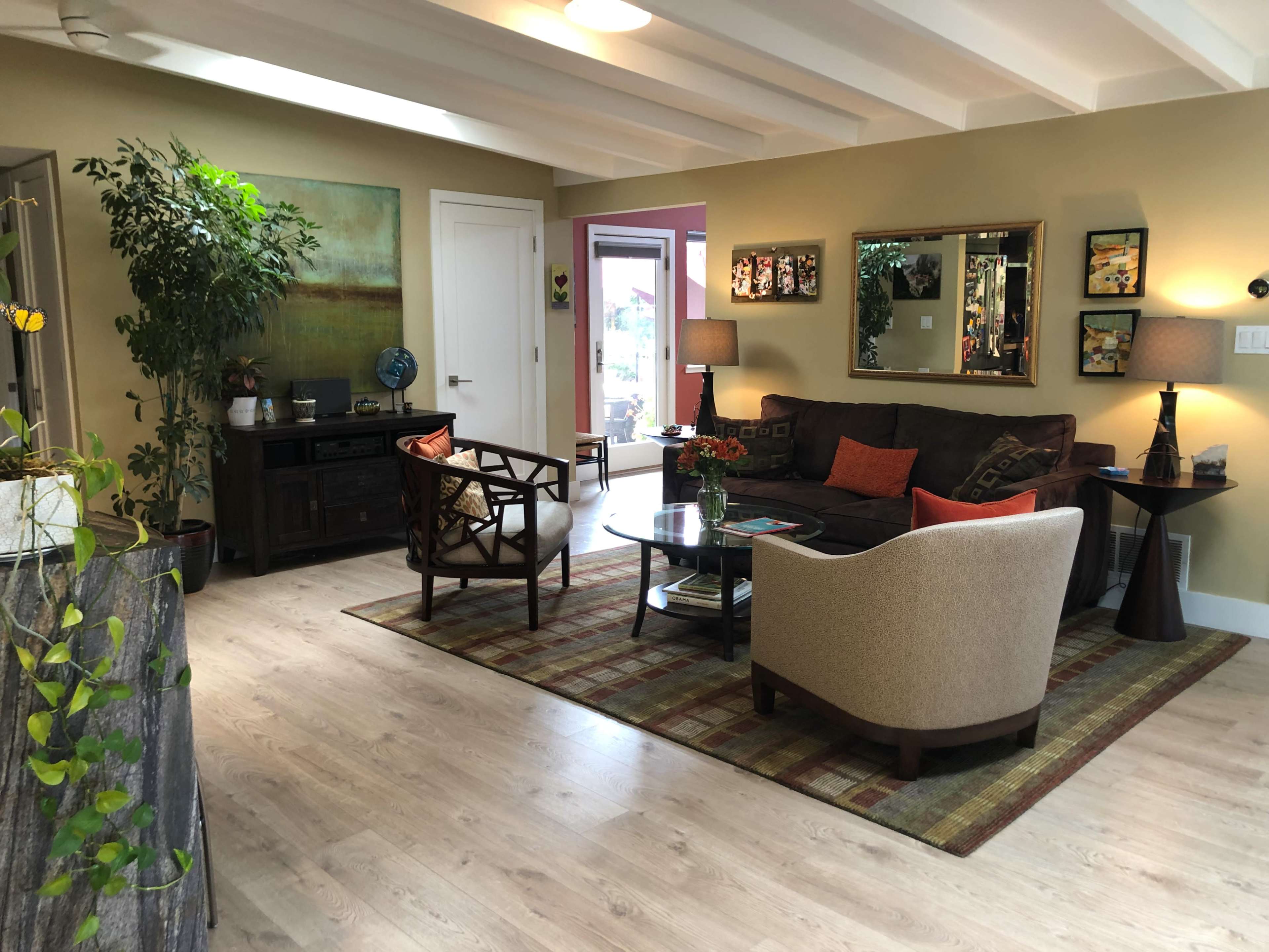 The living room features a sofa, armchair, and a coffee table, accompanied by plants and artwork on the walls.