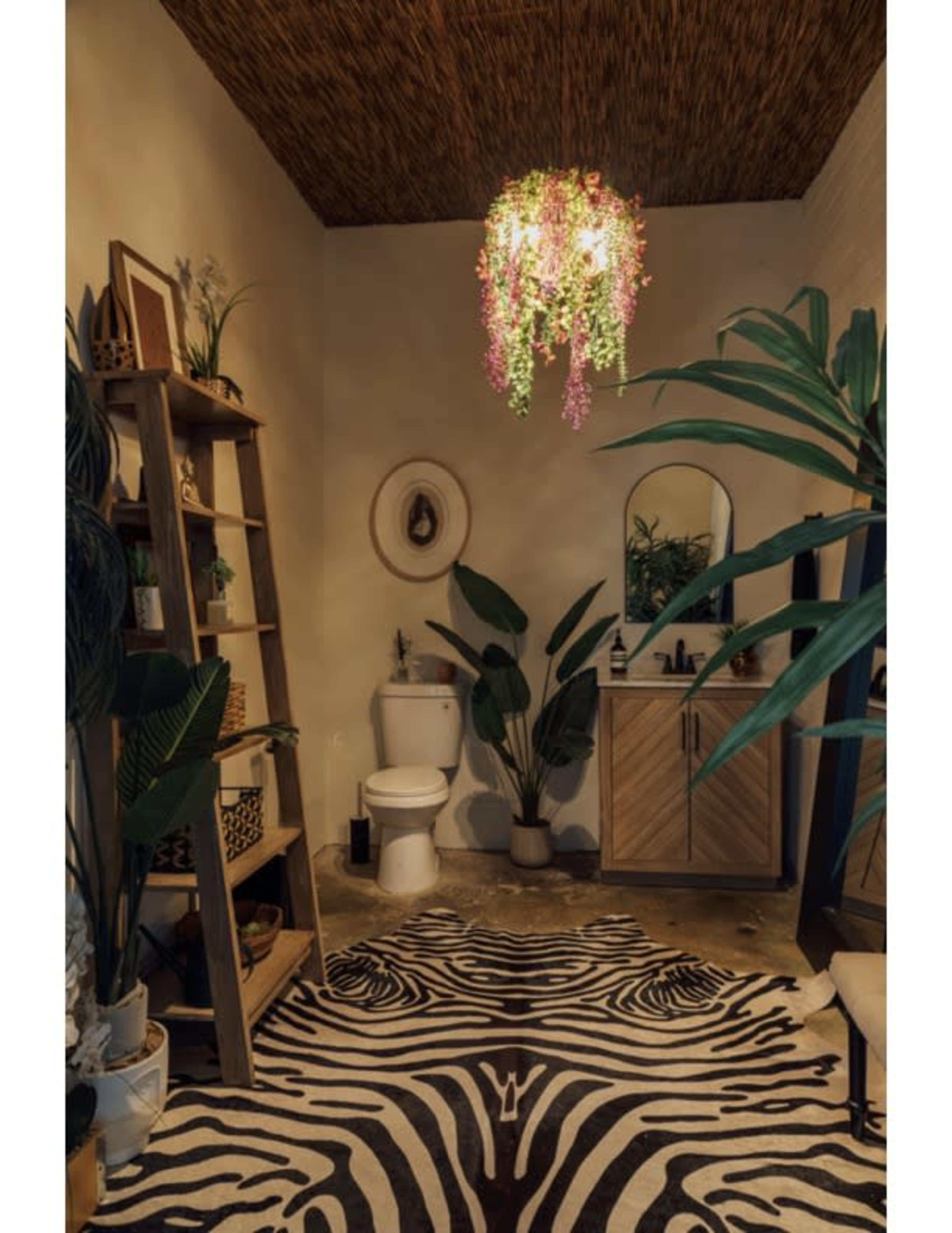 The image shows a stylish bathroom featuring a toilet, a wooden vanity with a mirror, a decorative plant, and a zebra-striped rug on the floor.