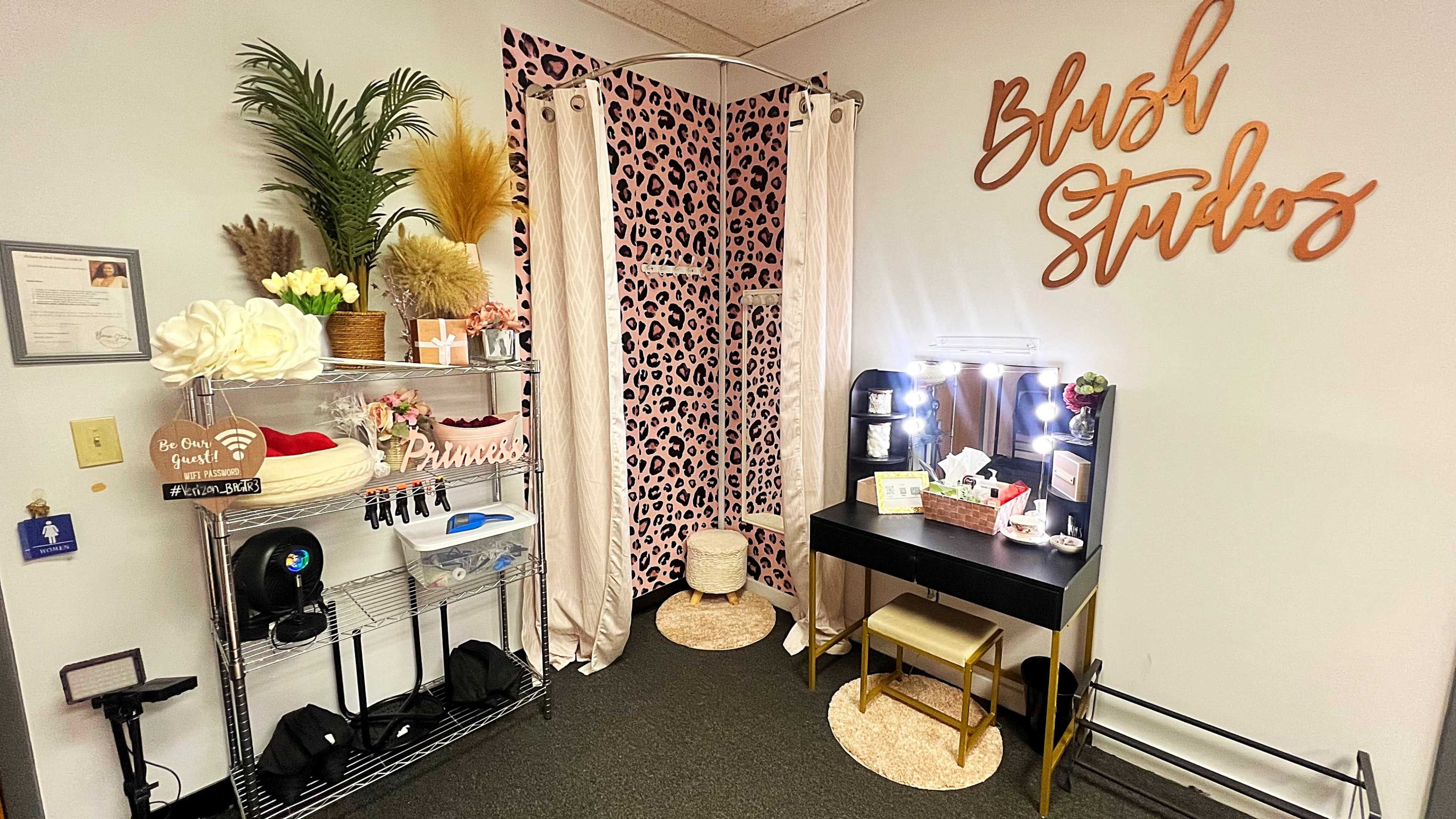 A small makeup studio features a mirrored vanity, shelving with beauty products, and a leopard print backdrop.