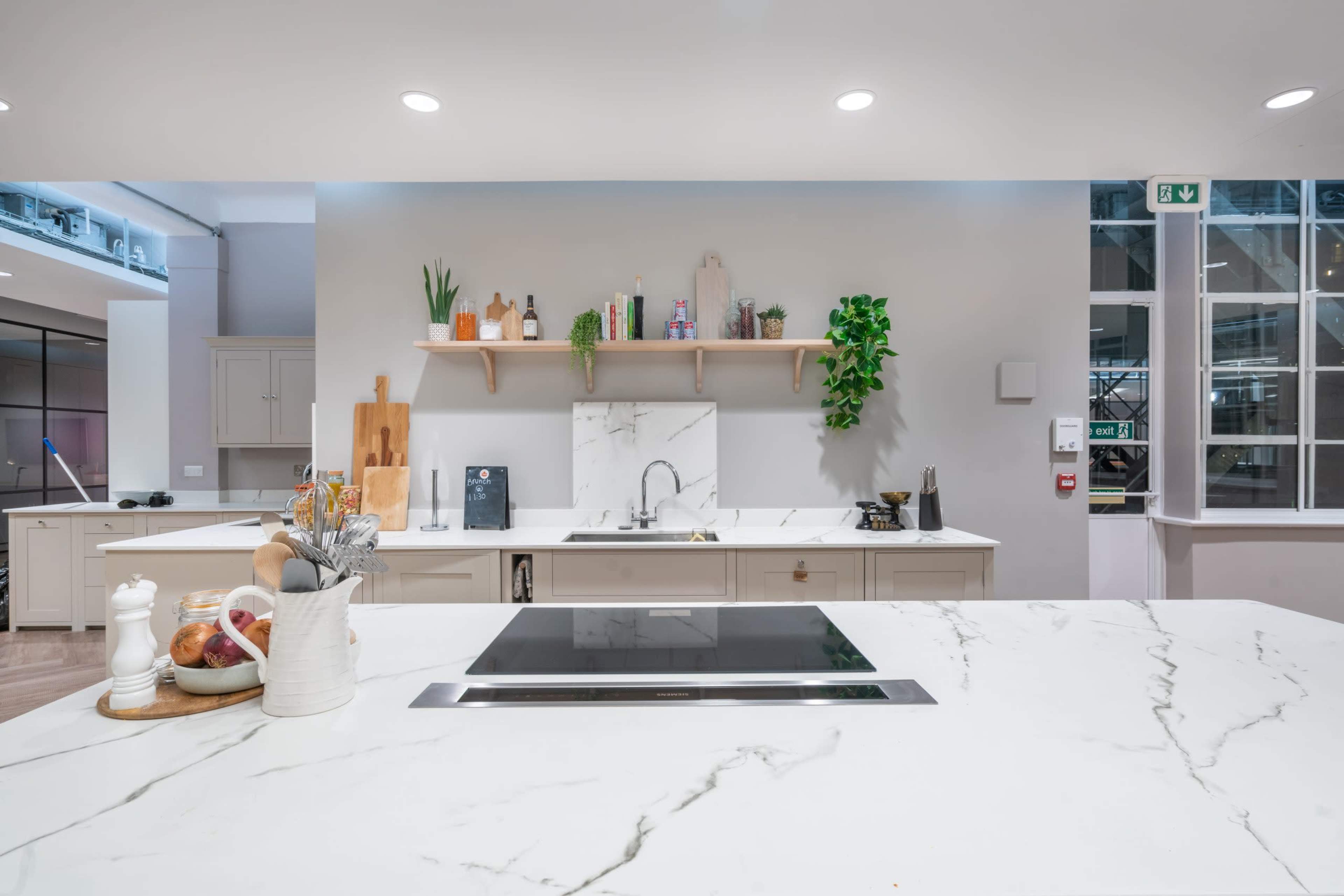 The image shows a modern kitchen with a white marble countertop, a sleek cooktop, and open shelves displaying various kitchen items.