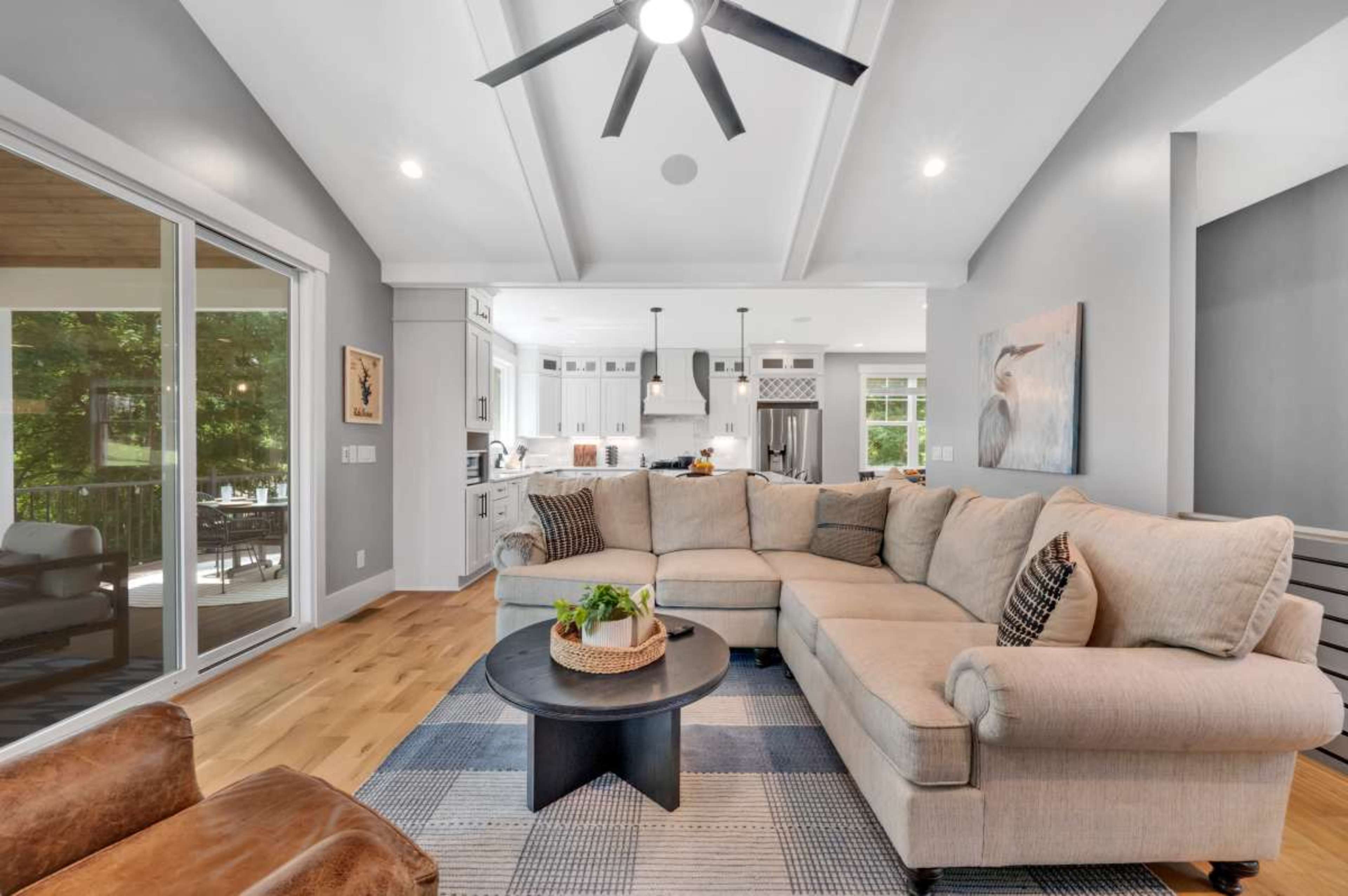 A spacious living room features a large sectional sofa, a circular coffee table, and a view of a well-lit kitchen area with modern appliances.