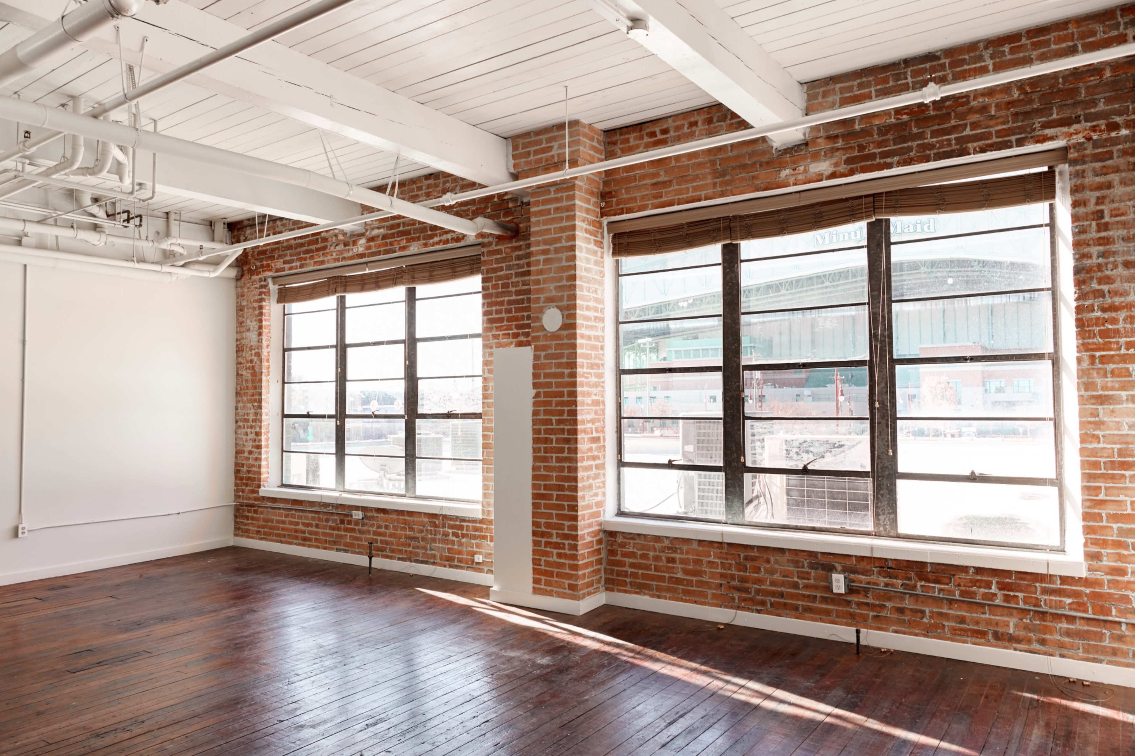 A spacious interior with exposed brick walls, large windows, and wooden flooring.