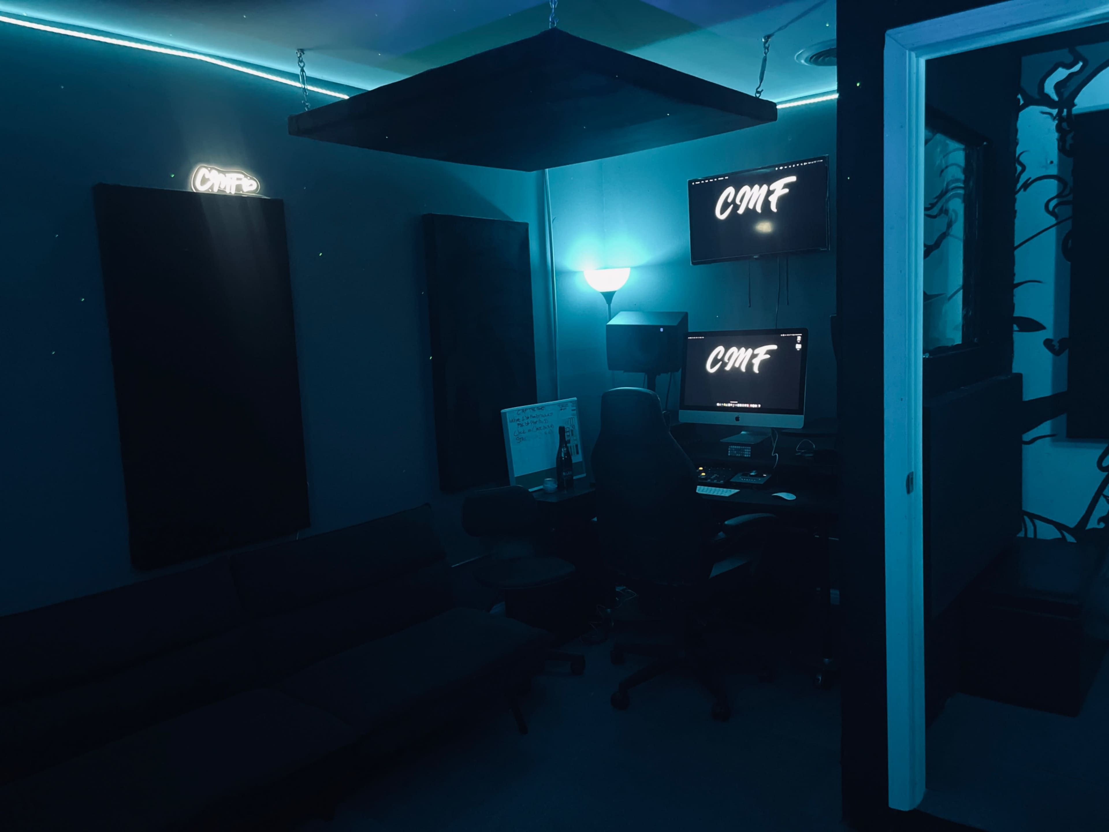 The image shows a dimly lit room featuring a desk with a computer, a couch, and black soundproof panels on the walls.