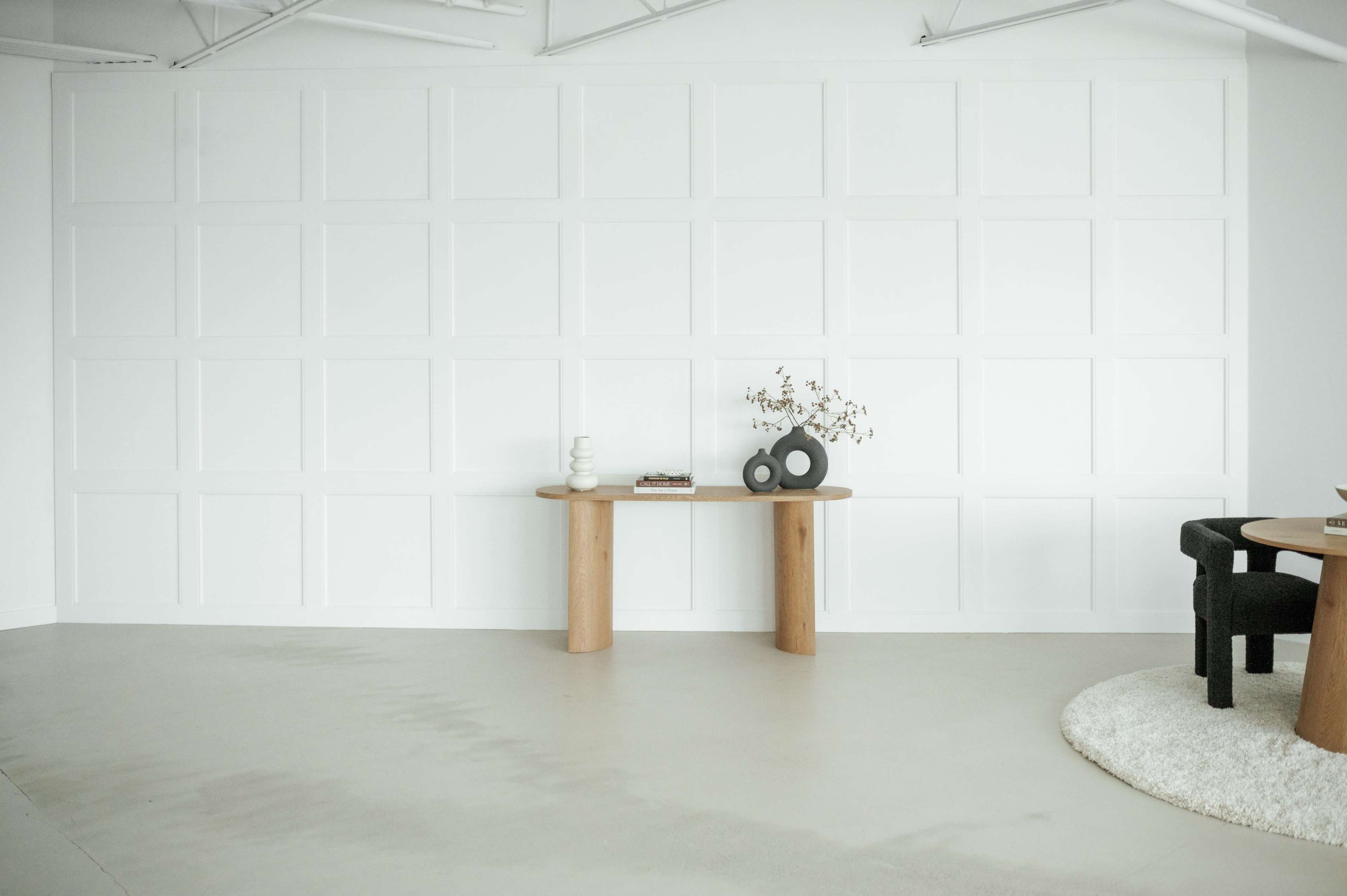 A minimalist interior space features a light-colored wall with a grid panel design and a simple wooden table displaying decor items.