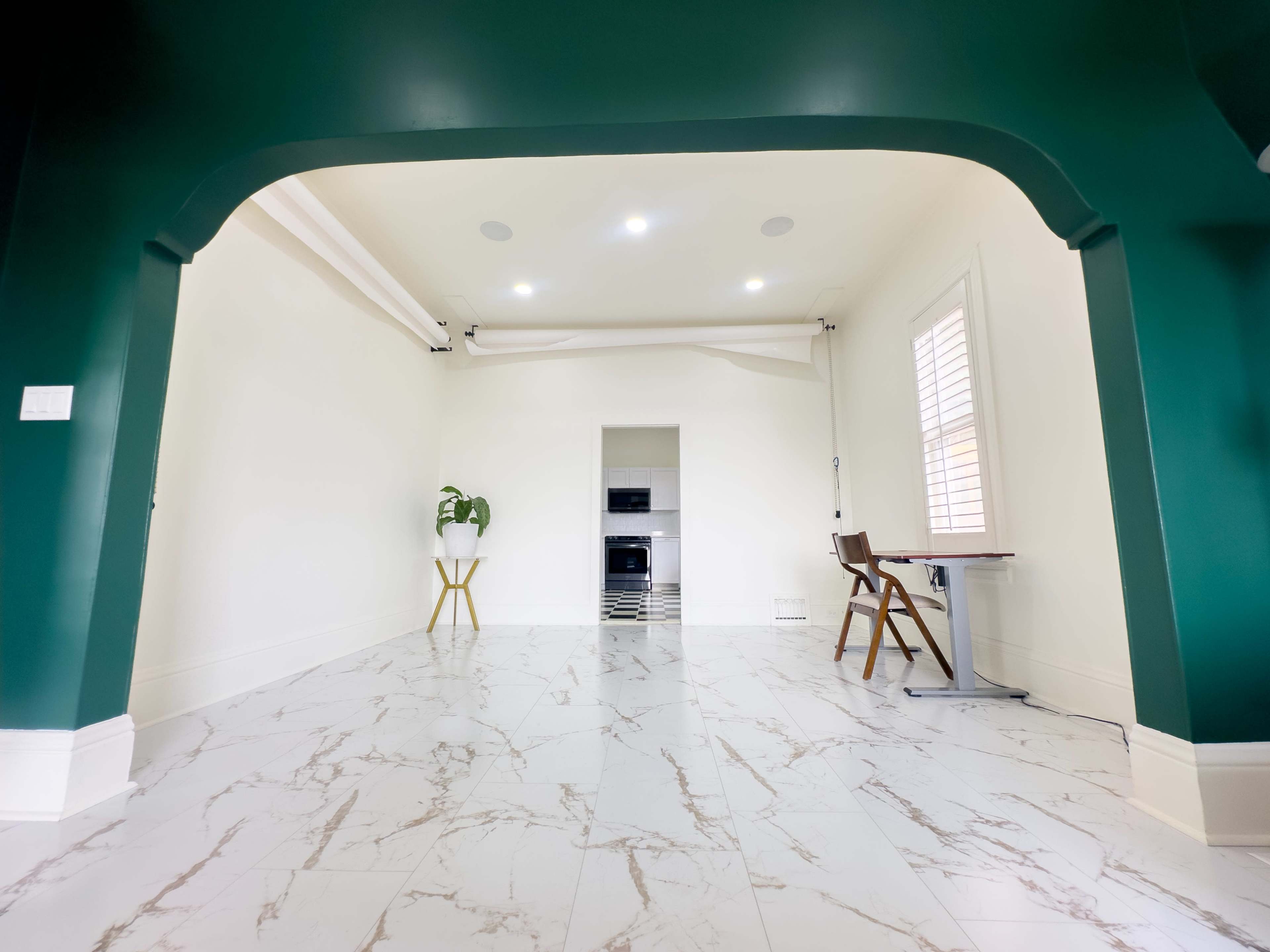 A room with green walls, a marble-patterned floor, and a small kitchen area visible in the background.