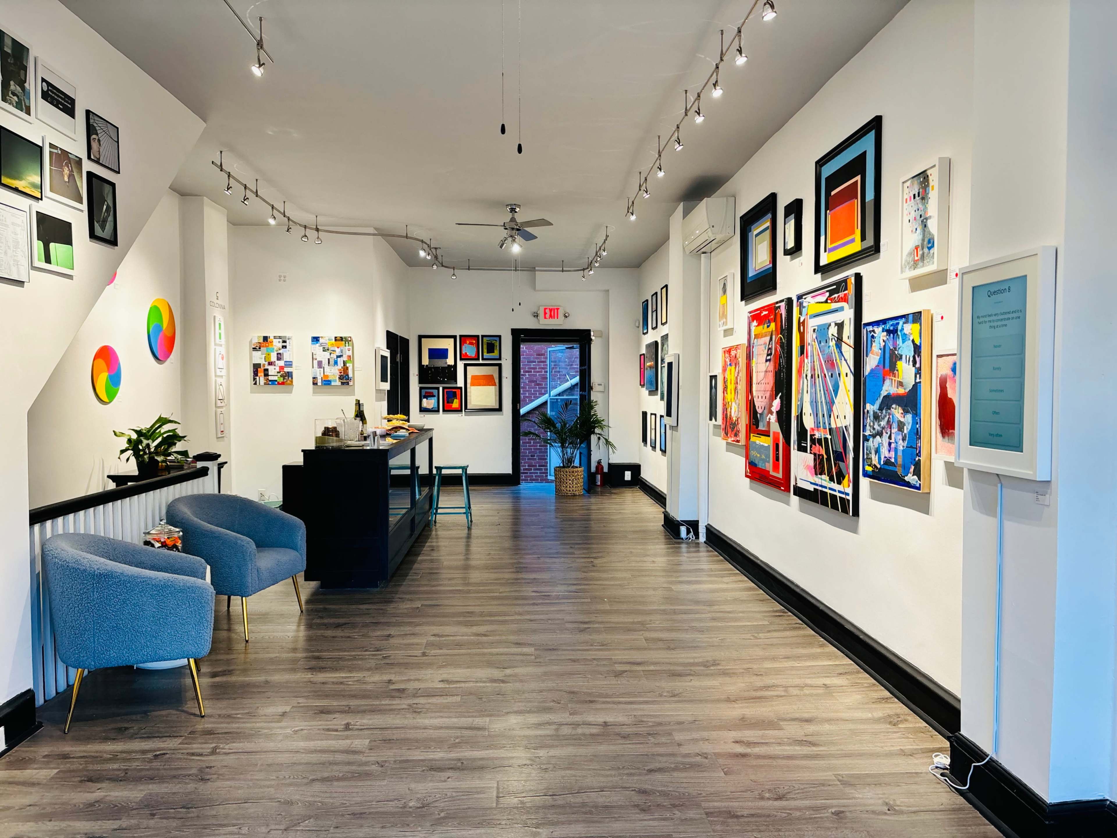 A modern art gallery with white walls adorned with various colorful artworks and two blue chairs positioned in the foreground.