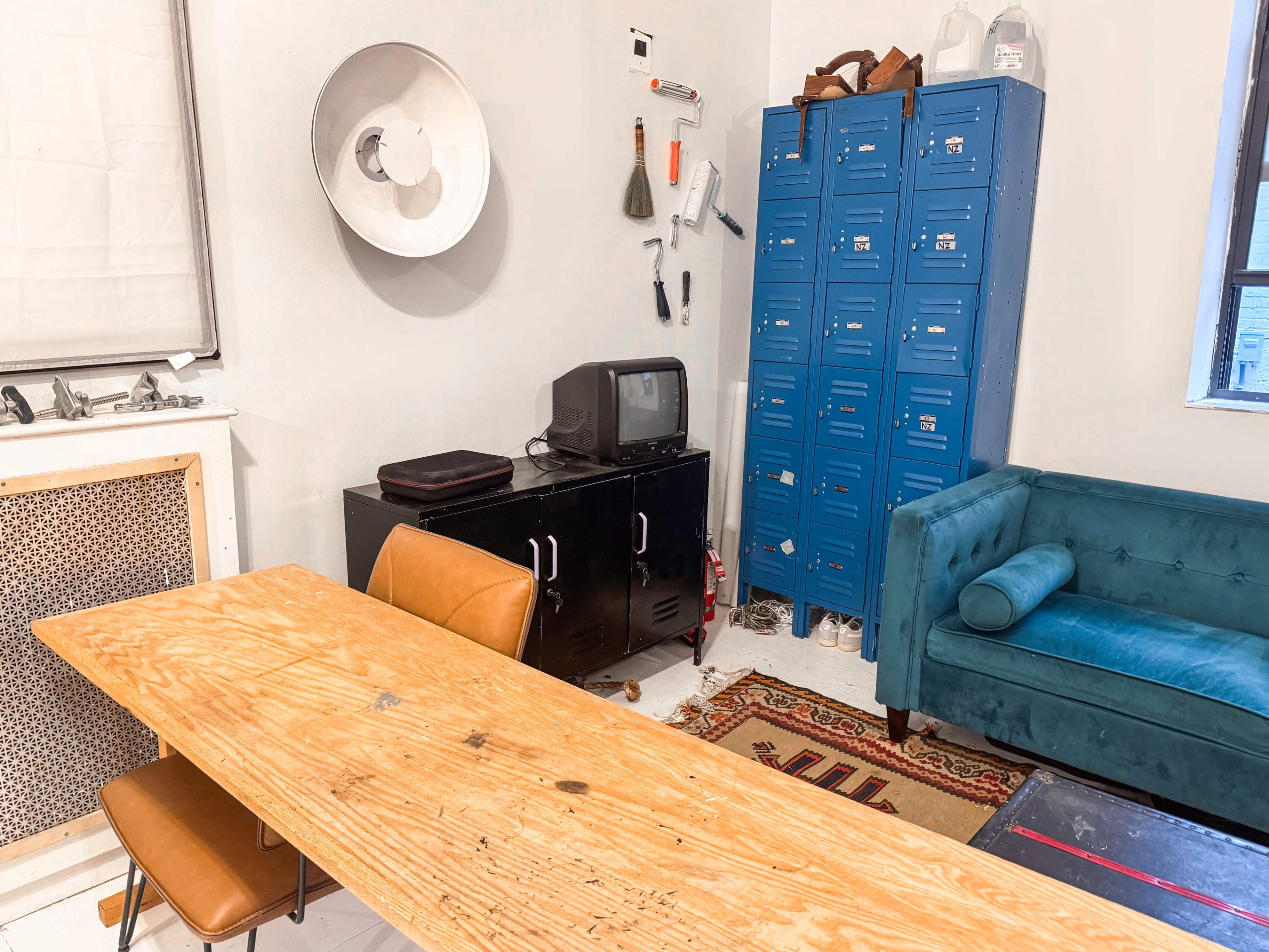 The image shows a room with a wooden table, two brown chairs, a black cabinet, a blue locker unit, an old-style television, and a teal sofa.
