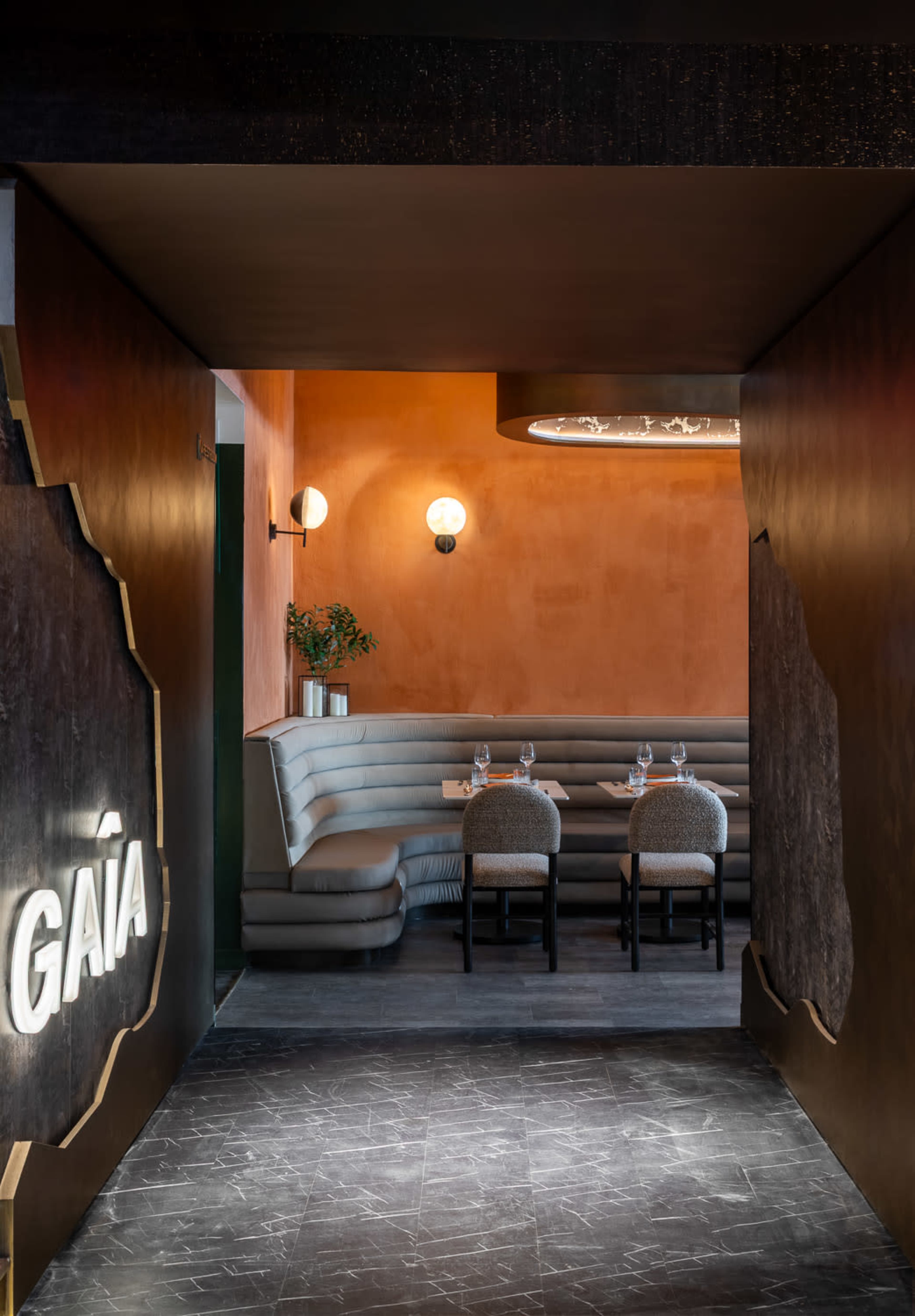 A modern restaurant entrance features a stylish hallway with a prominent illuminated sign and a dining area in soft hues.