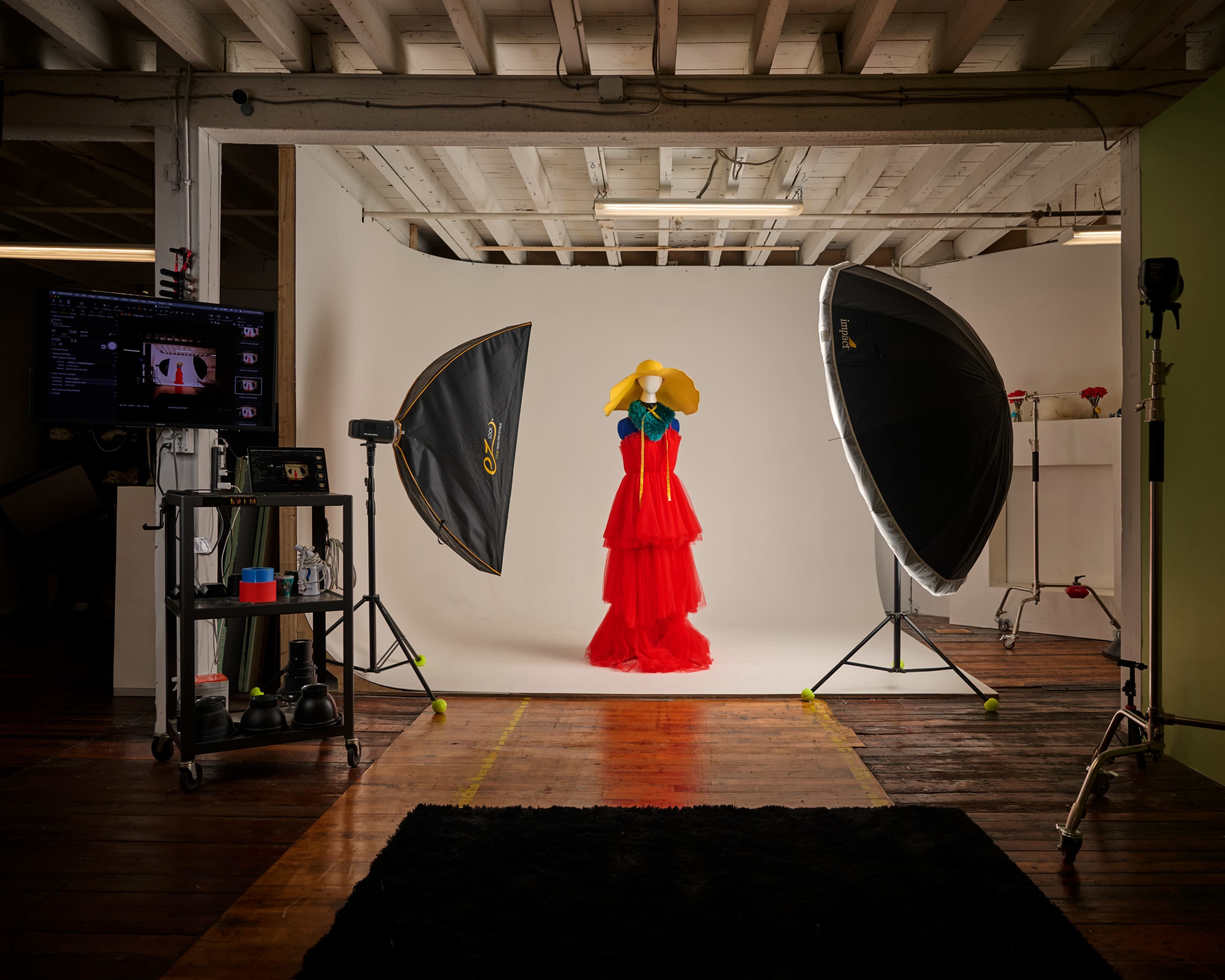 A red dress on a mannequin is showcased in a well-lit photography studio surrounded by large softbox lights and a backdrop.