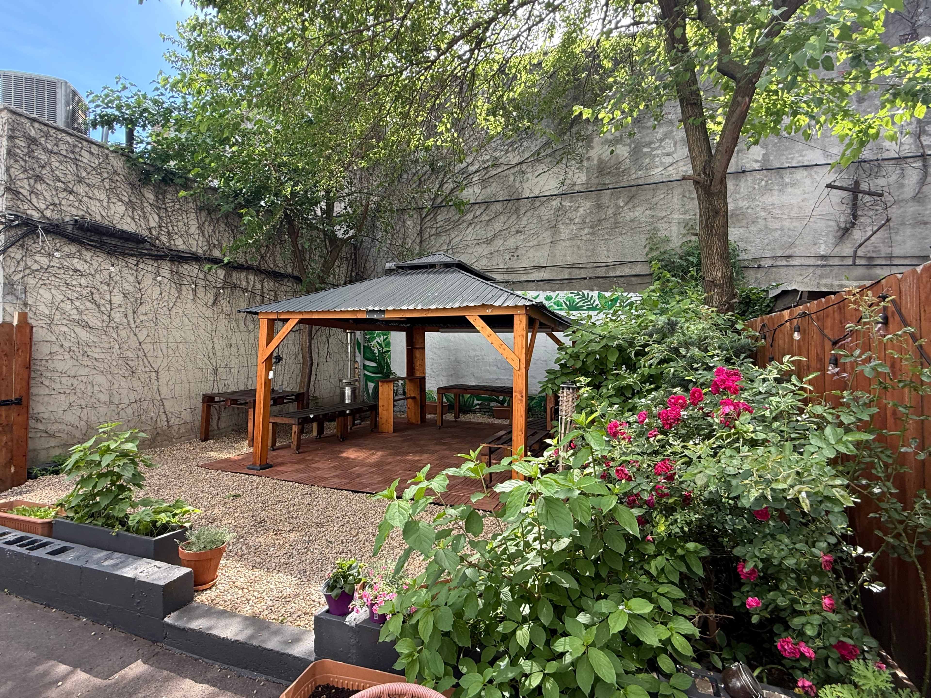 The image shows a garden area with a wooden gazebo surrounded by plants and gravel pathways.