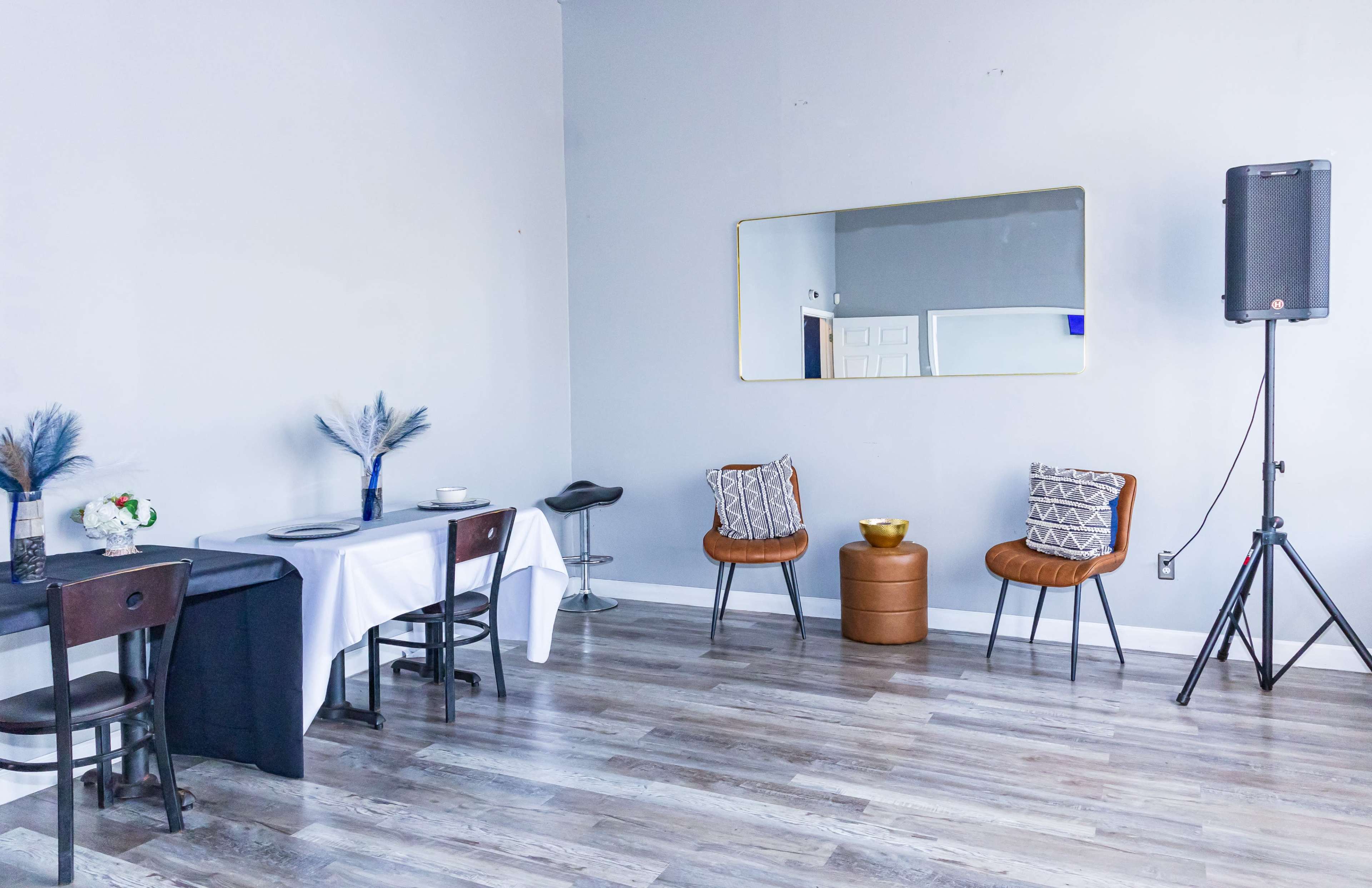 The image shows a minimalistic interior space with two seating areas, a table set for dining, and a large mirror on the wall.