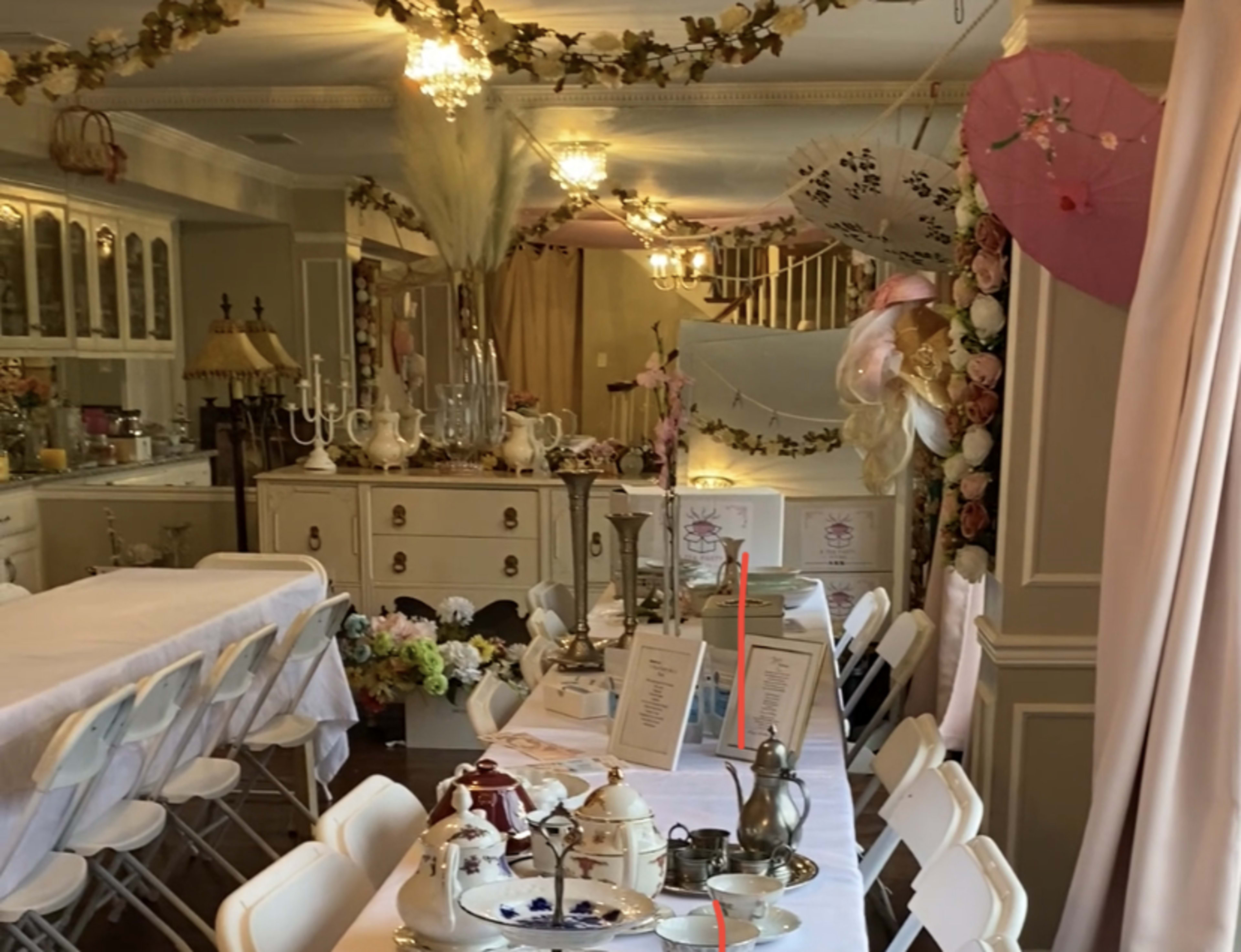 A decorated dining area with a long table set for a gathering, featuring floral arrangements and various tableware.