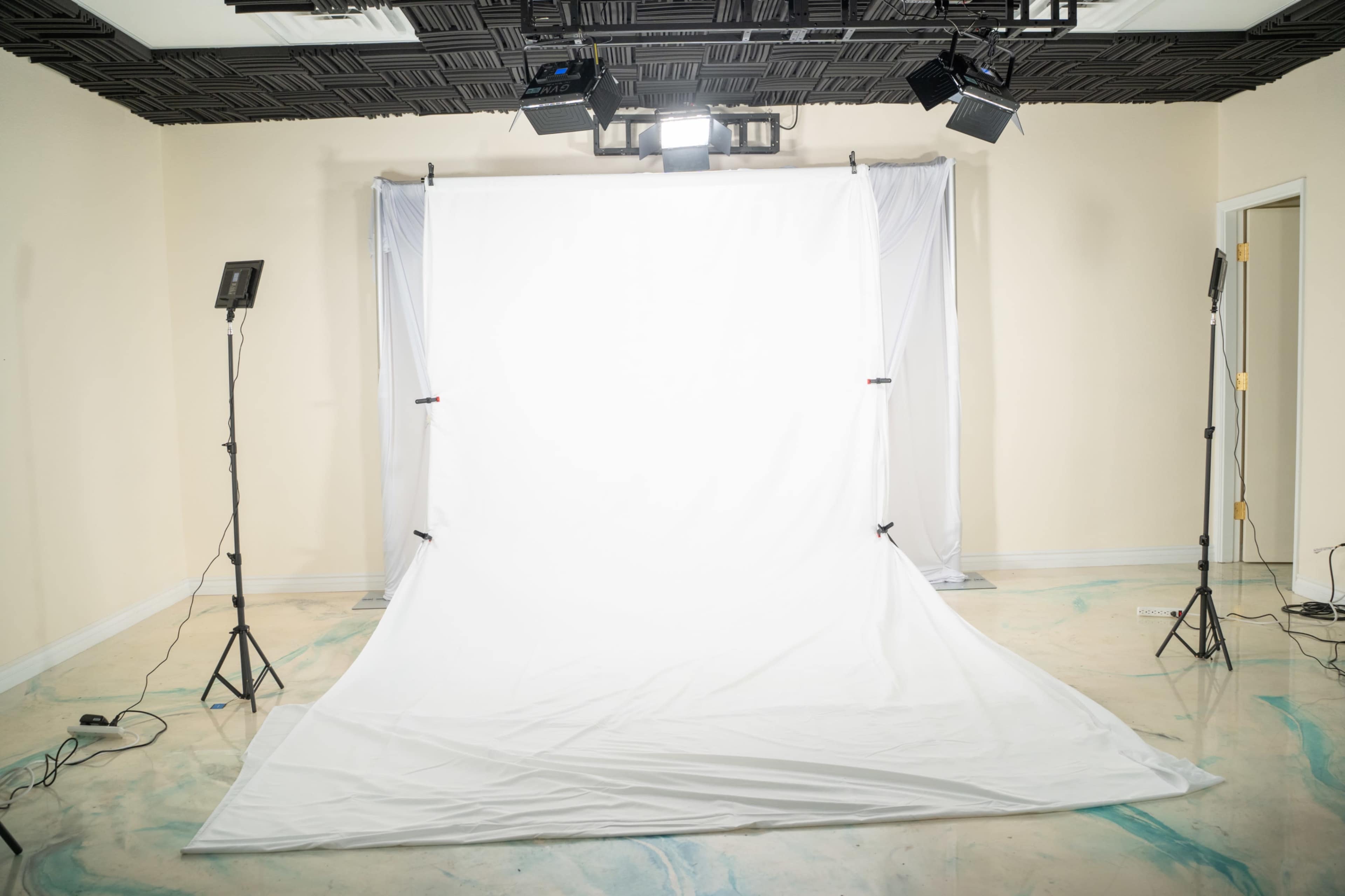 A photography studio features a large white backdrop set up with lighting fixtures on stands.