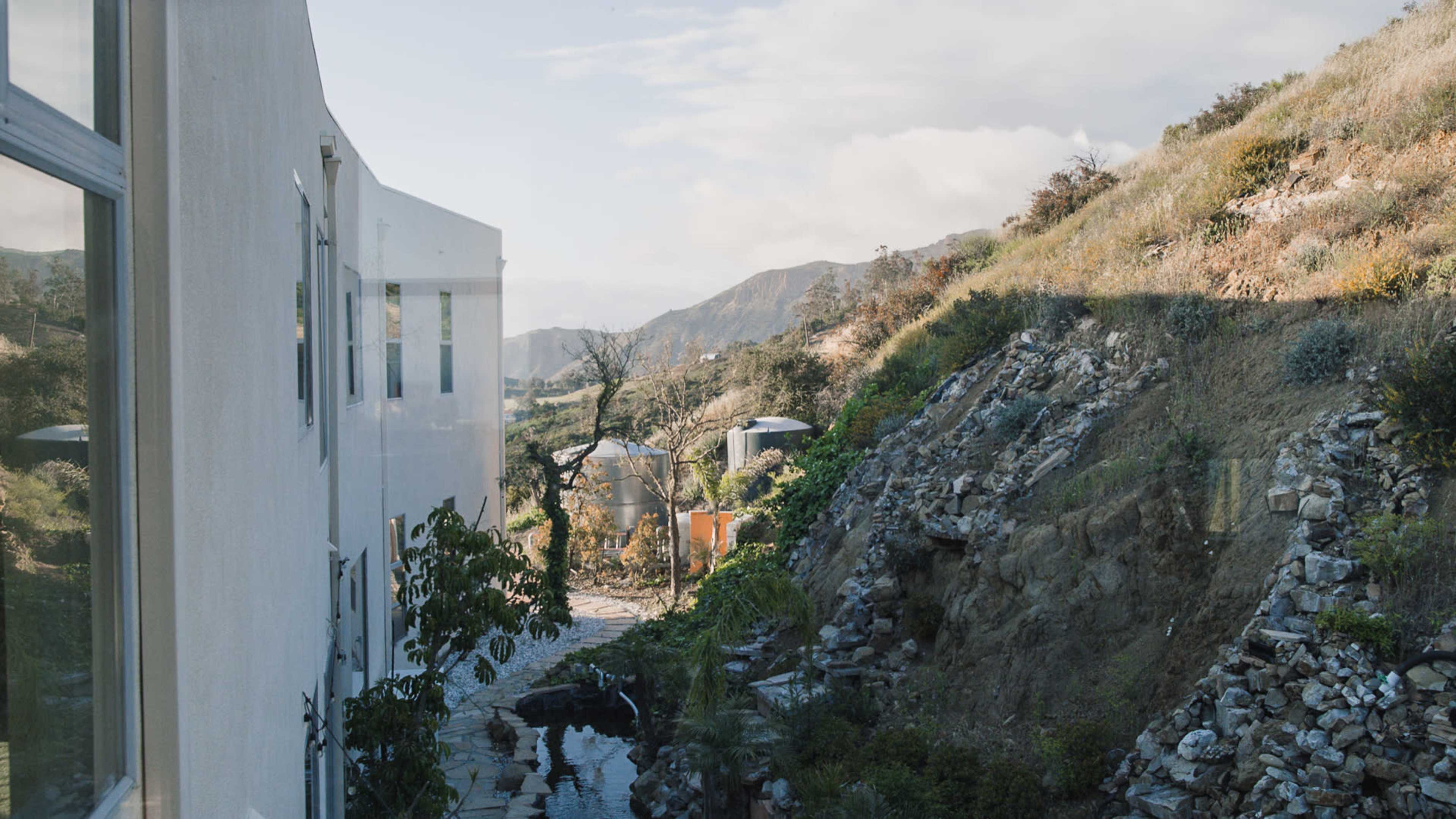 A modern building overlooks a rocky slope and a landscaped path leading down to a mountain valley.