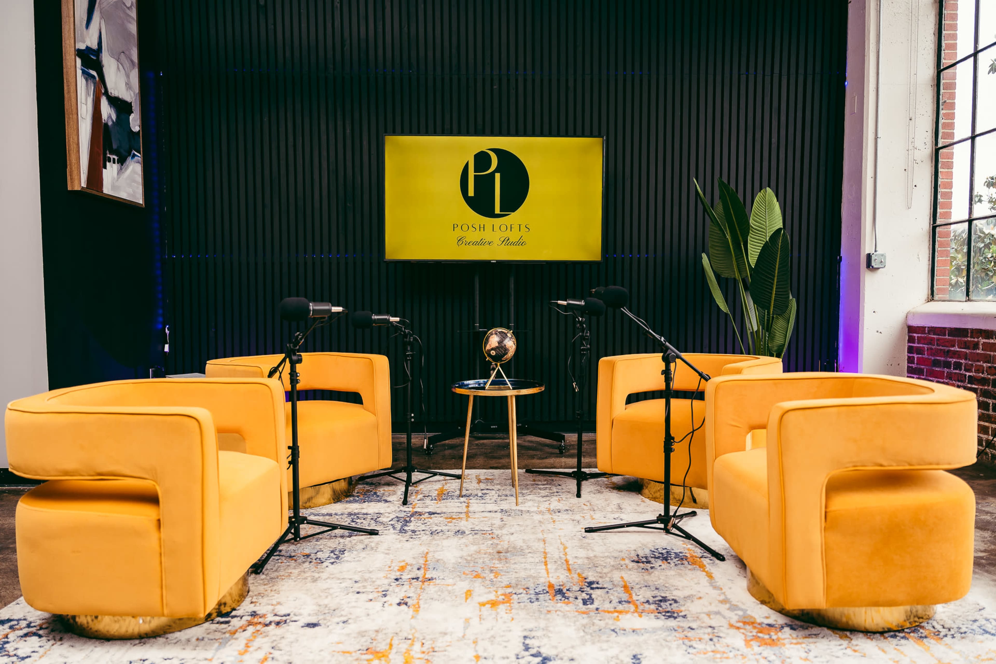 The image shows a modern interview setup with four yellow chairs arranged around a small table, a microphone on each side, and a large screen displaying the "Posh Lots" logo in the background.