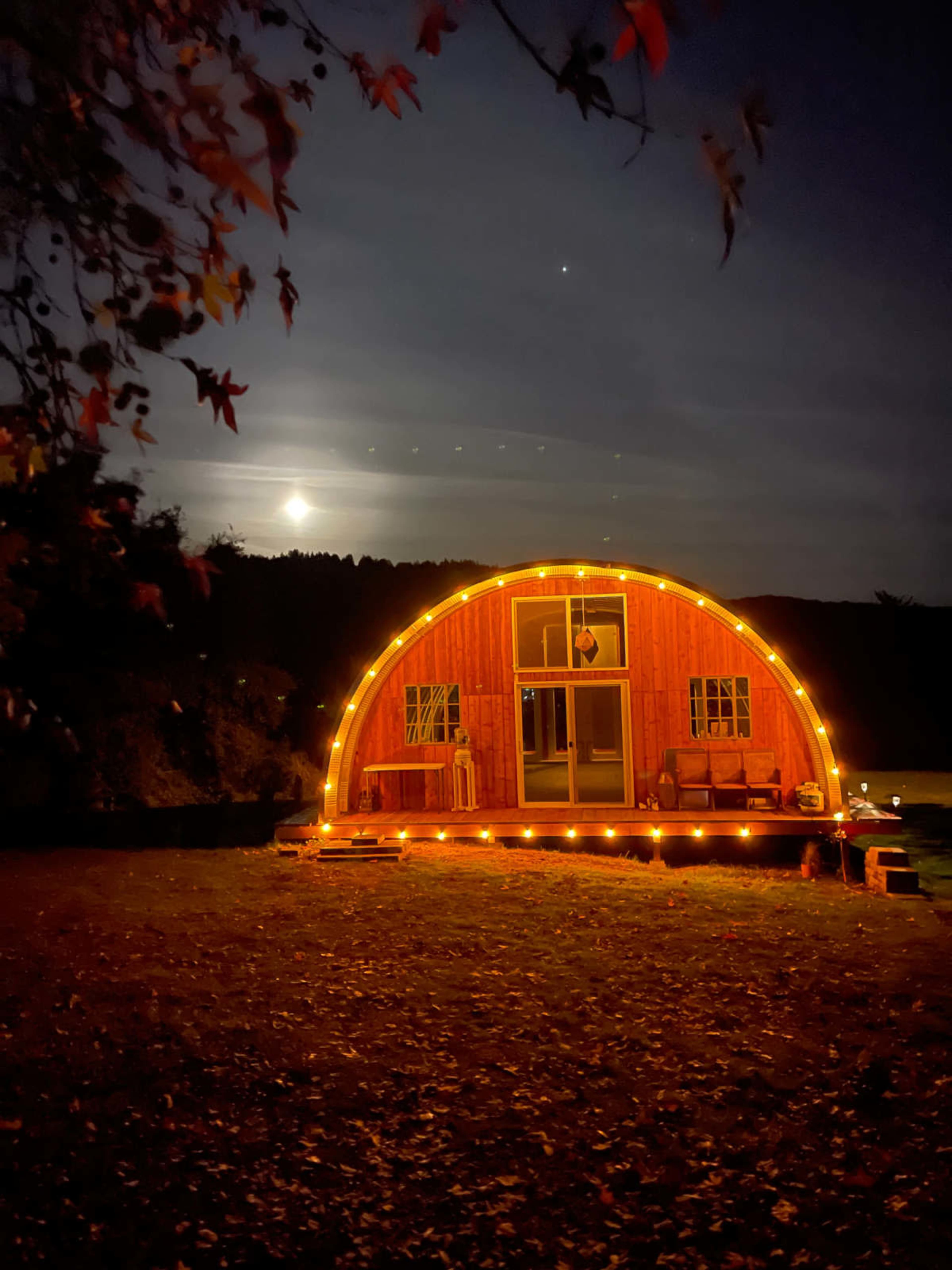 A red, curved building with lights outlines its exterior, set against a night sky with a visible moon.