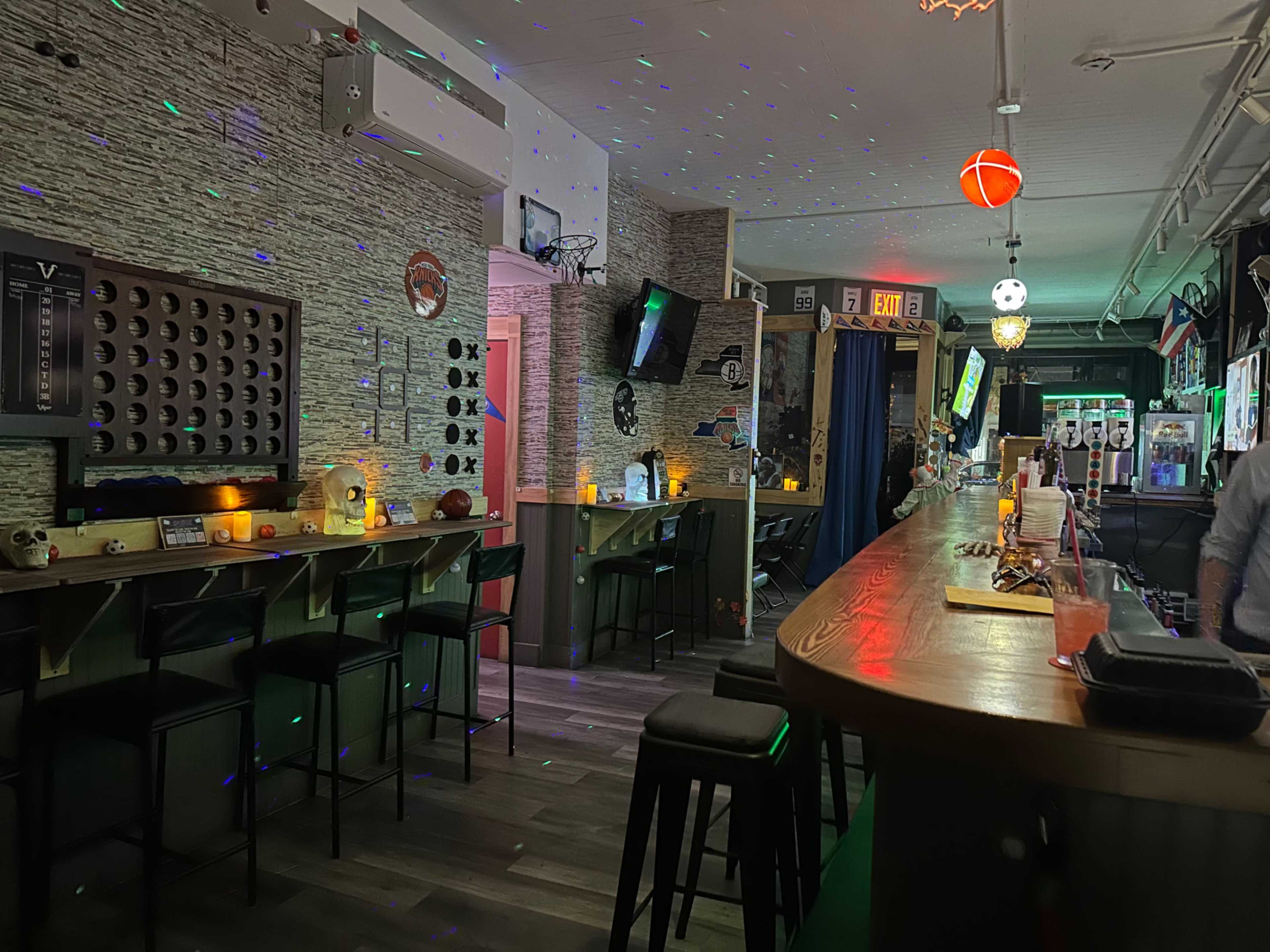 The image shows a dimly lit bar with a long countertop, high stools, and colorful lights casting patterns on the walls.