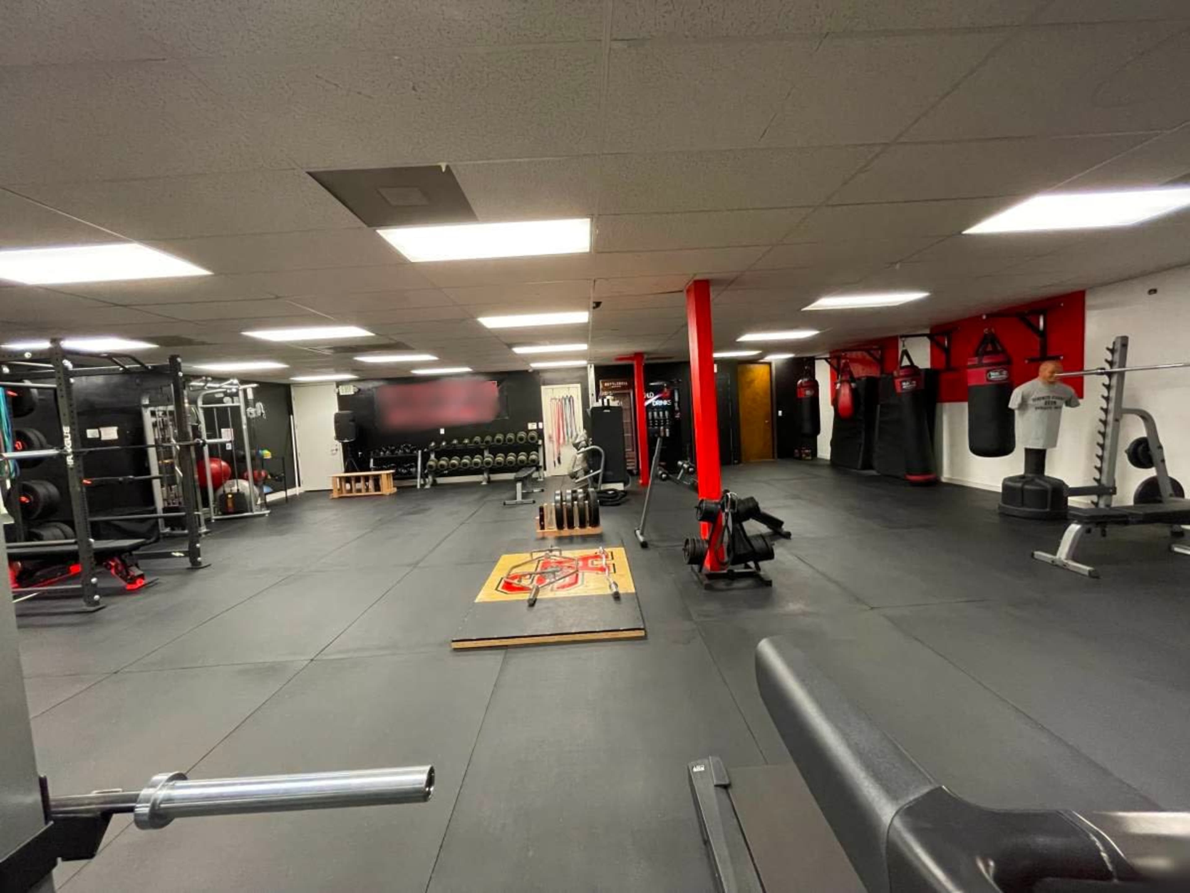 An interior view of a fitness gym featuring various exercise equipment, weight racks, and punching bags arranged in a spacious layout.