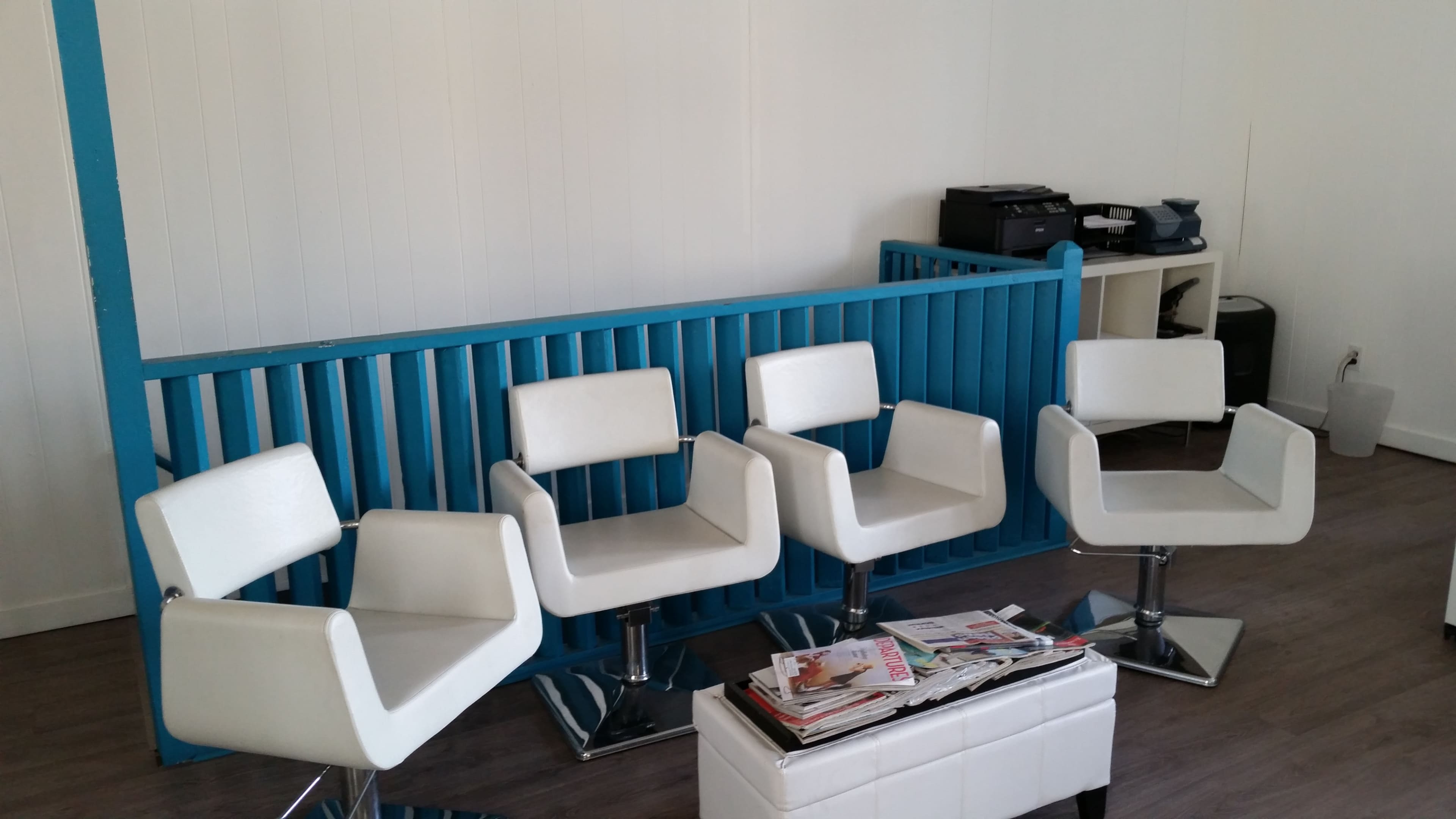 Four white swivel chairs arranged in front of a blue partition in a minimalist waiting area.