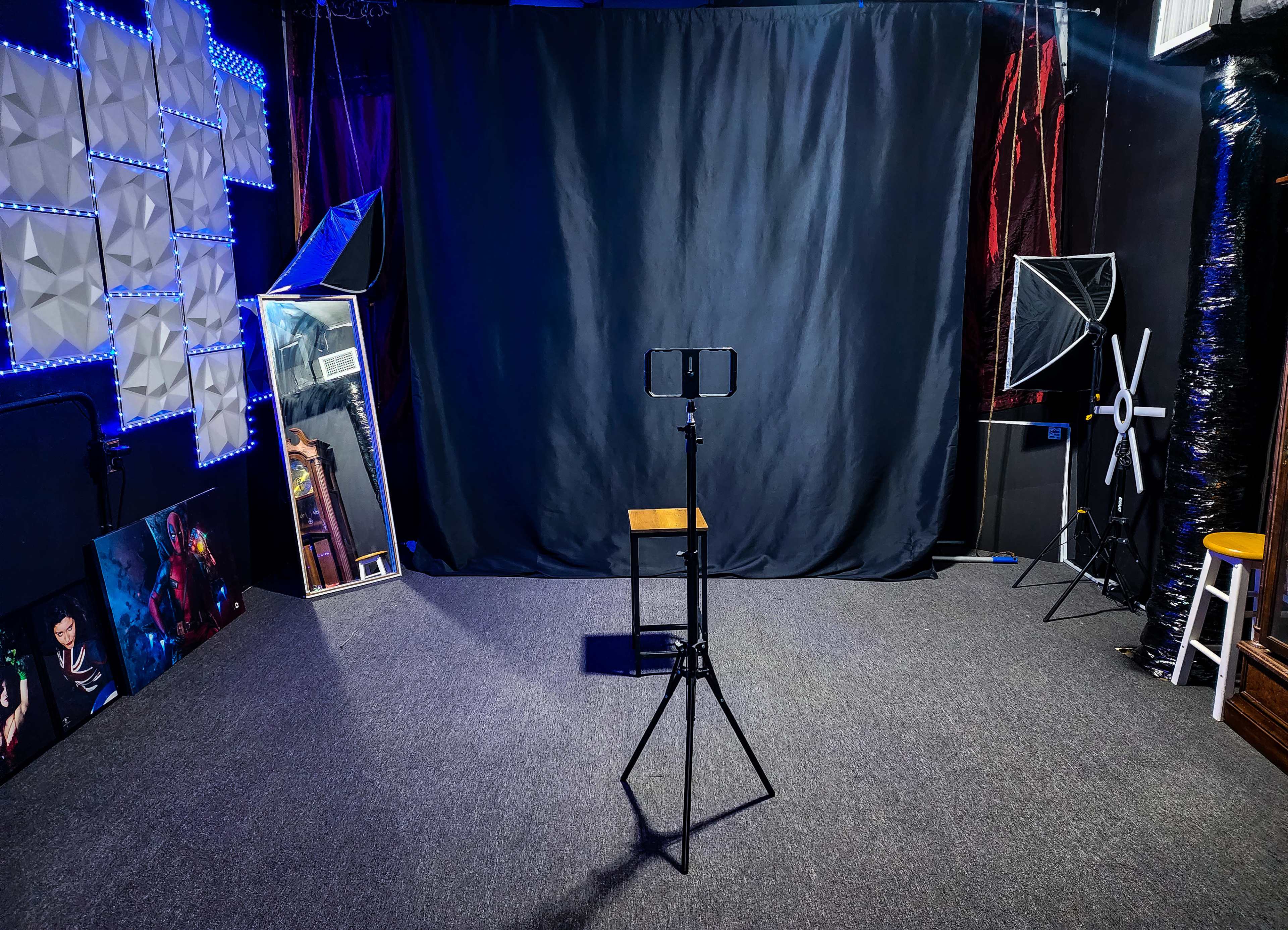 A photography studio with a black backdrop, a stool in the center, lighting equipment, a mirror, and various decorations on the walls.