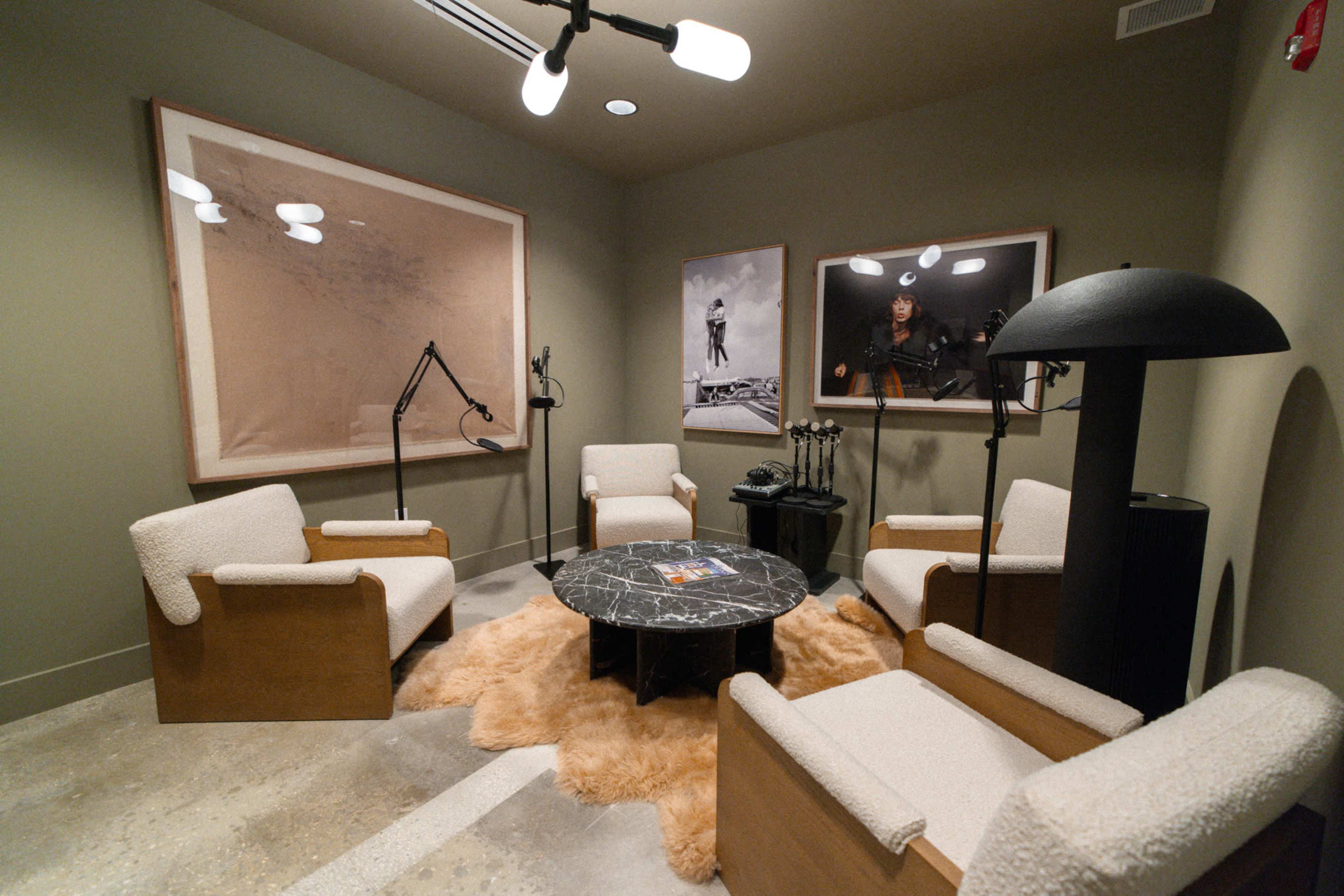 The image shows a modern seating area with four upholstered chairs, a round marble table at the center, and two large framed photographs on the walls.