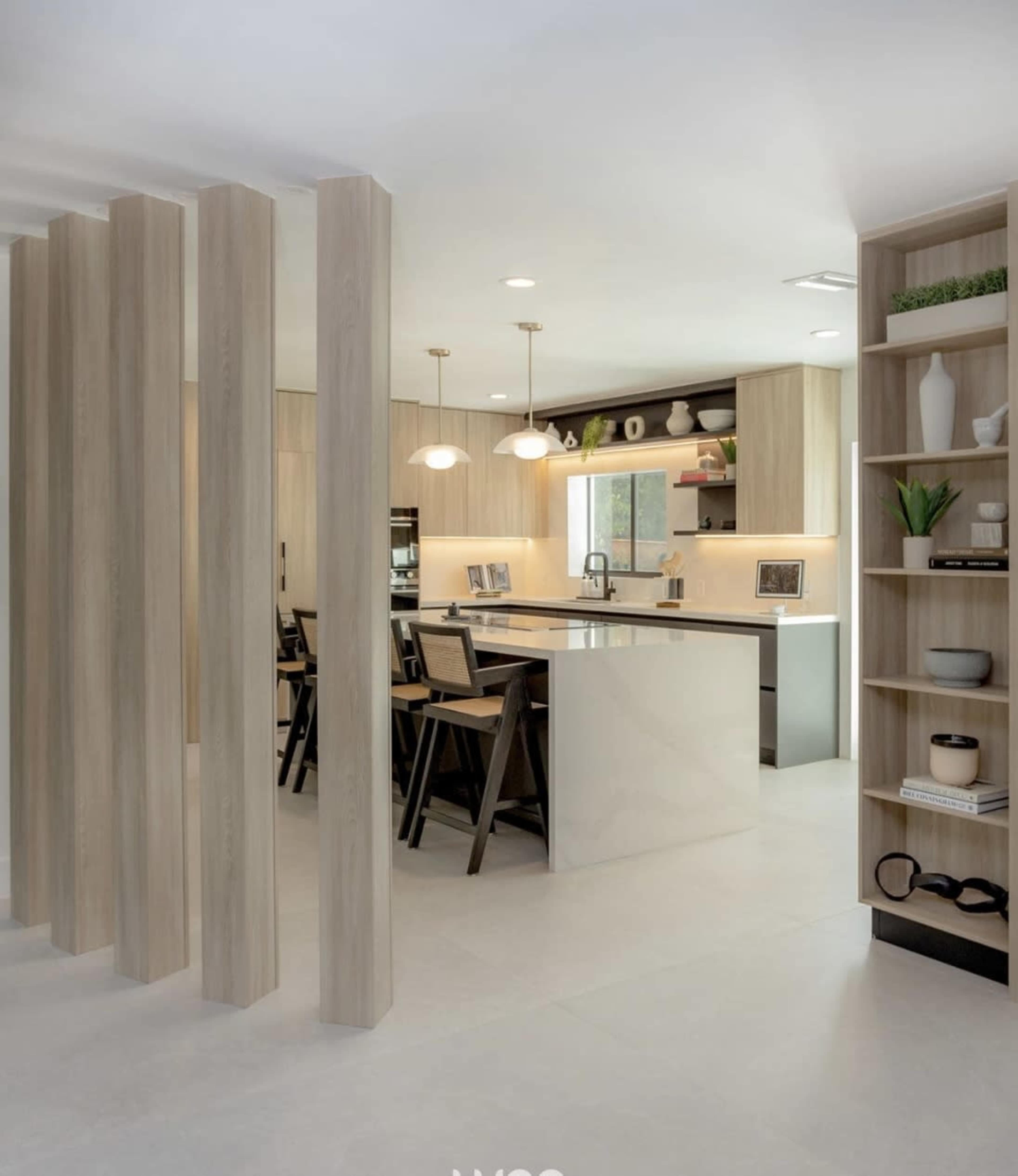 A modern kitchen and dining area feature wooden pillars, sleek cabinetry, and an island with seating.