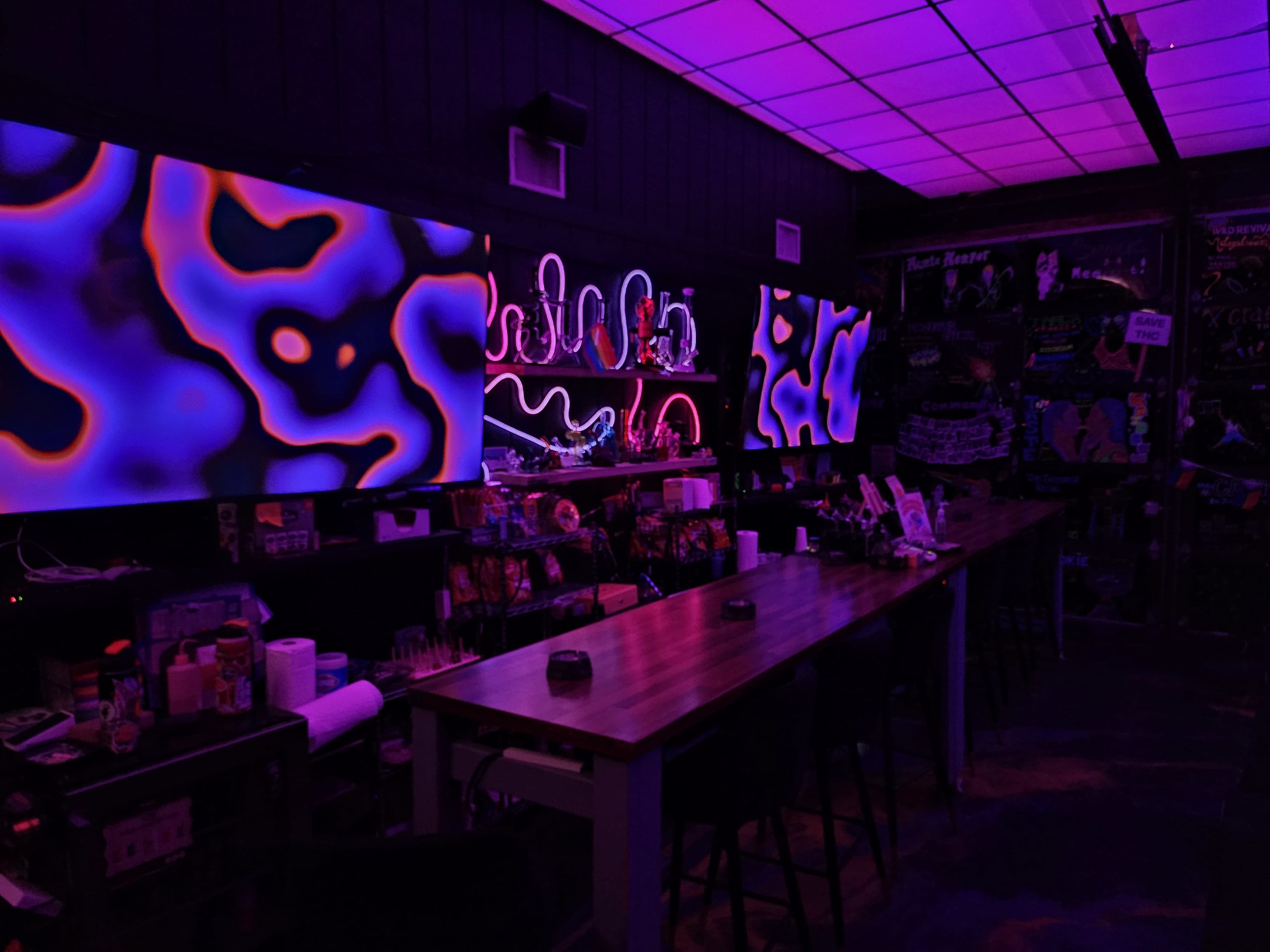 The image shows a dimly lit bar area with vibrant, colorful abstract patterns displayed on screens along the wall.