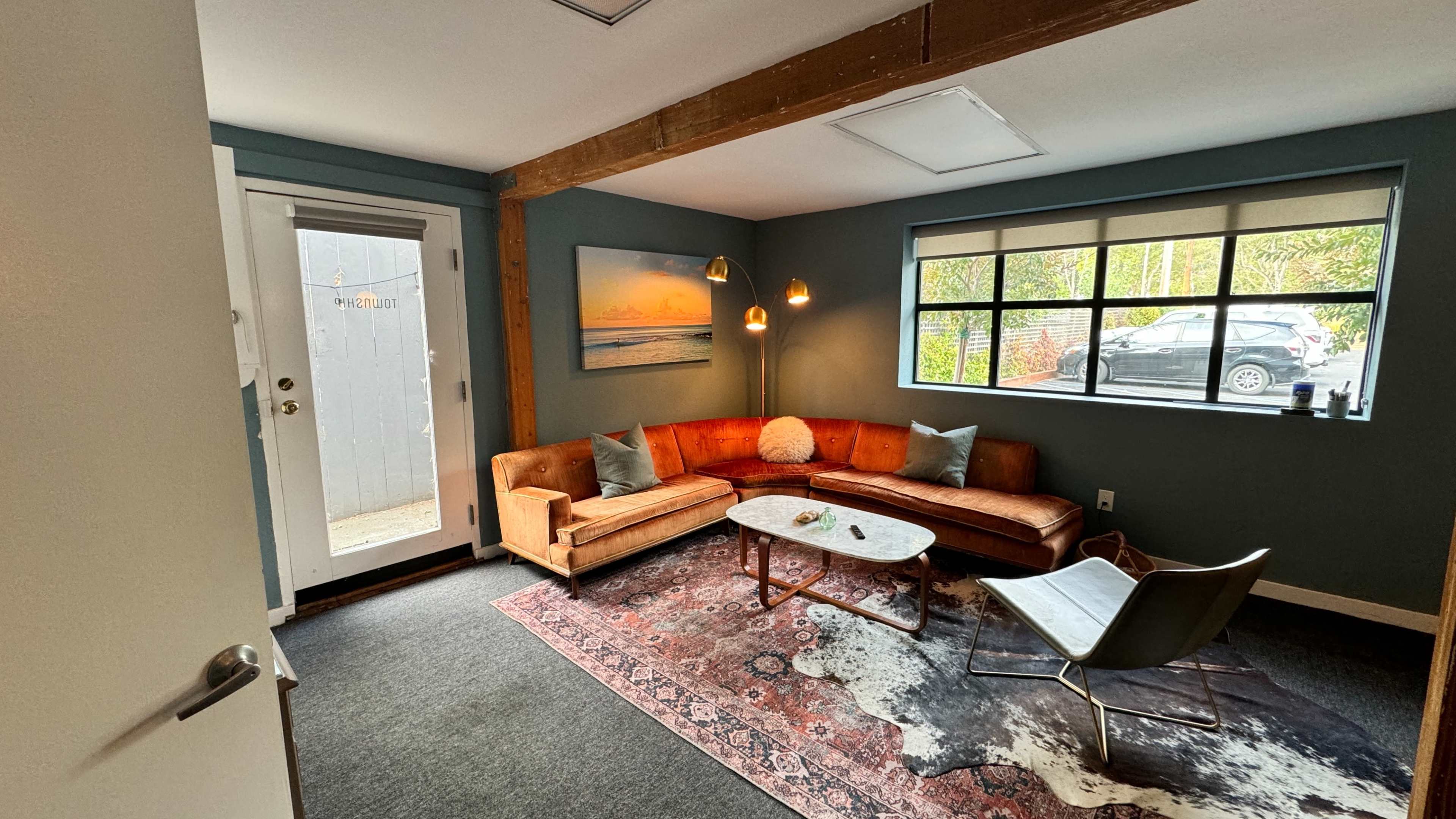 A cozy living room with a brown sofa, a glass coffee table, a chair, and a door leading outside.
